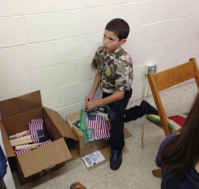Boy standing beside a box of folded striped clothes in a room with a tiled floor and white wall