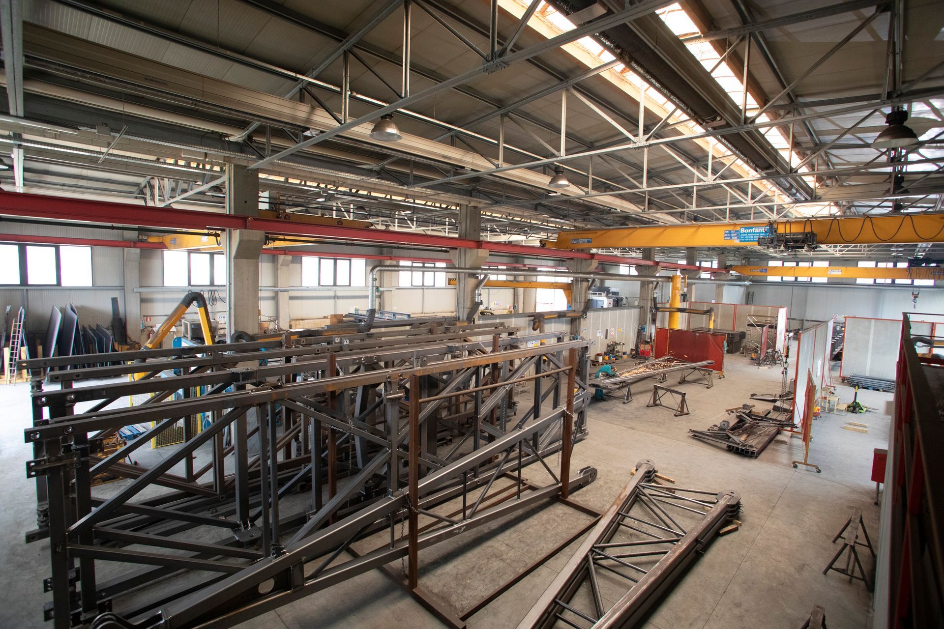 Veduta grandangolare degli interni di una grande officina di lavorazione dei metalli, con capriate e macchinari industriali pesanti.
