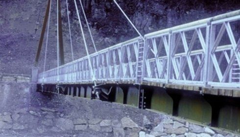 Una passerella sospesa con ringhiere triangolari bianche attraversa un paesaggio roccioso e irregolare.