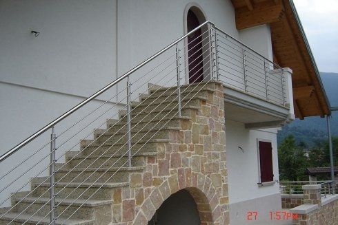 Scala esterna in pietra con ringhiera moderna in acciaio inossidabile che conduce a una porta su un edificio bianco.