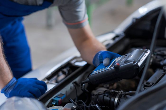 Mechanic in blue gloves inspecting a car engine with a diagnostic scanner under the hood