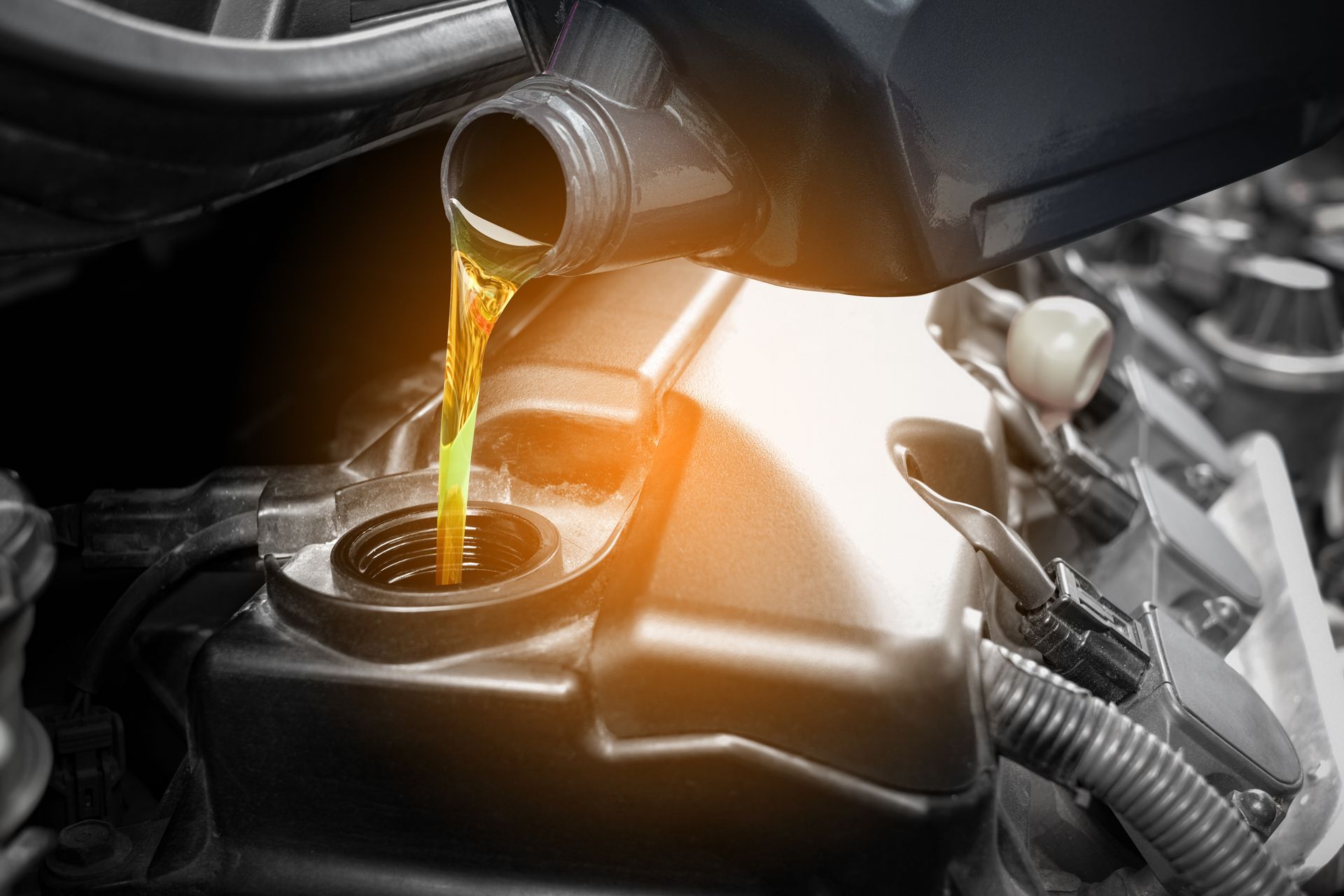 Motor oil pouring into a car engine, with warm light reflecting on the engine bay.