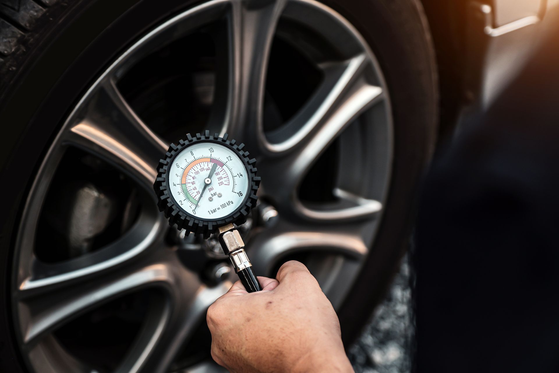 Hand checking tire pressure with a gauge on a car wheel