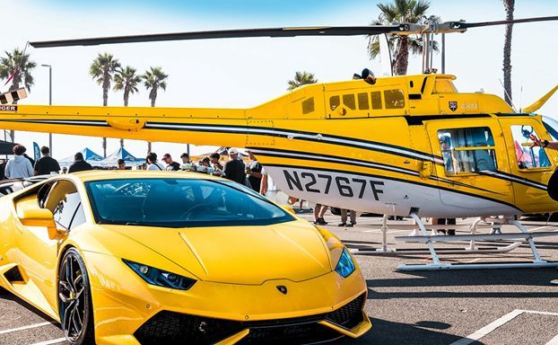Cars 'N Copters on the Coast A yellow lamborghini is parked next to a yellow helicopter in a parking lot.