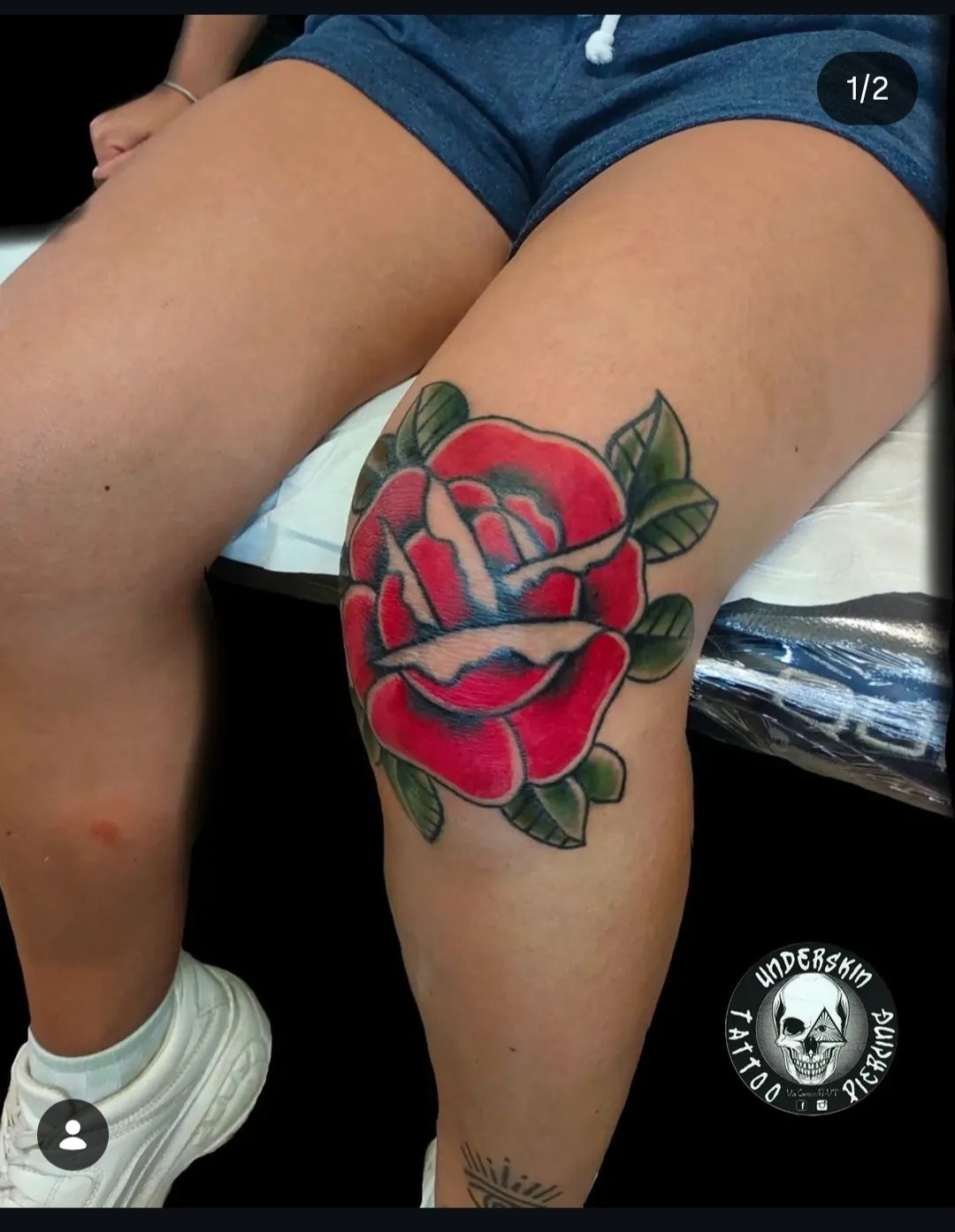 Tatuaggio sulla gamba di una rosa rossa con foglie verdi, raffigurante una persona seduta.