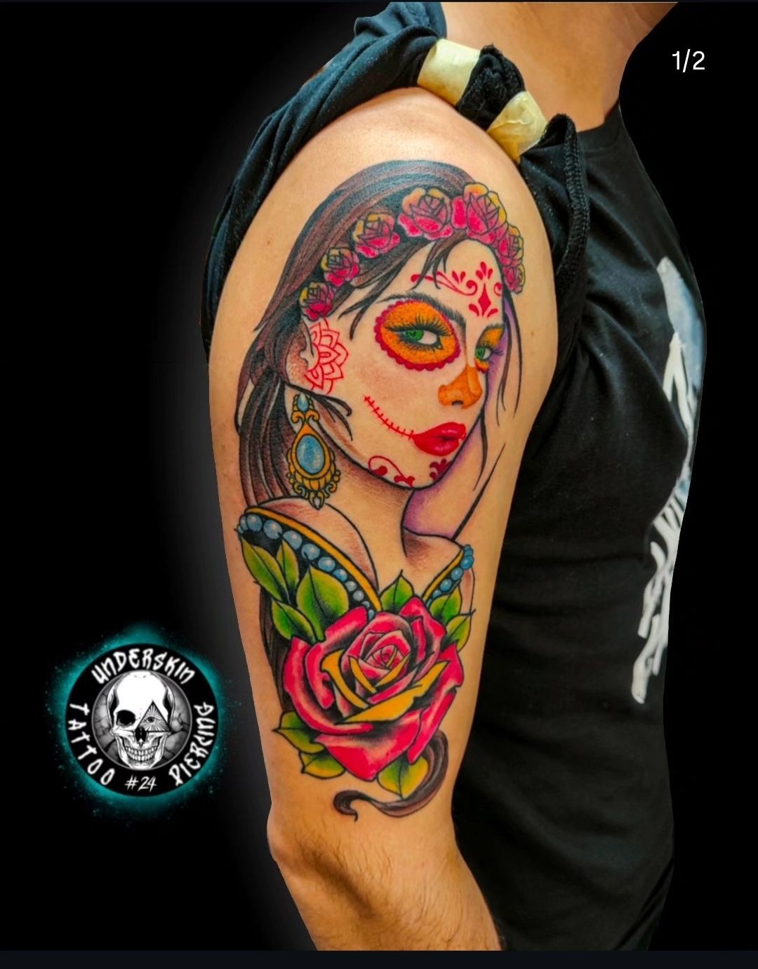 Primo piano di un tatuaggio di ritratto colorato sulla parte superiore del braccio, con fiori rosa e labbra rosso acceso.