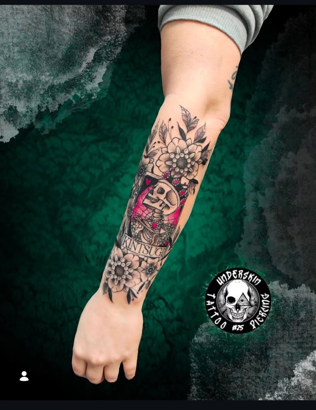 Un tatuaggio sull'avambraccio con un teschio centrale incorniciato da motivi floreali, elementi geometrici e un bagliore rosa