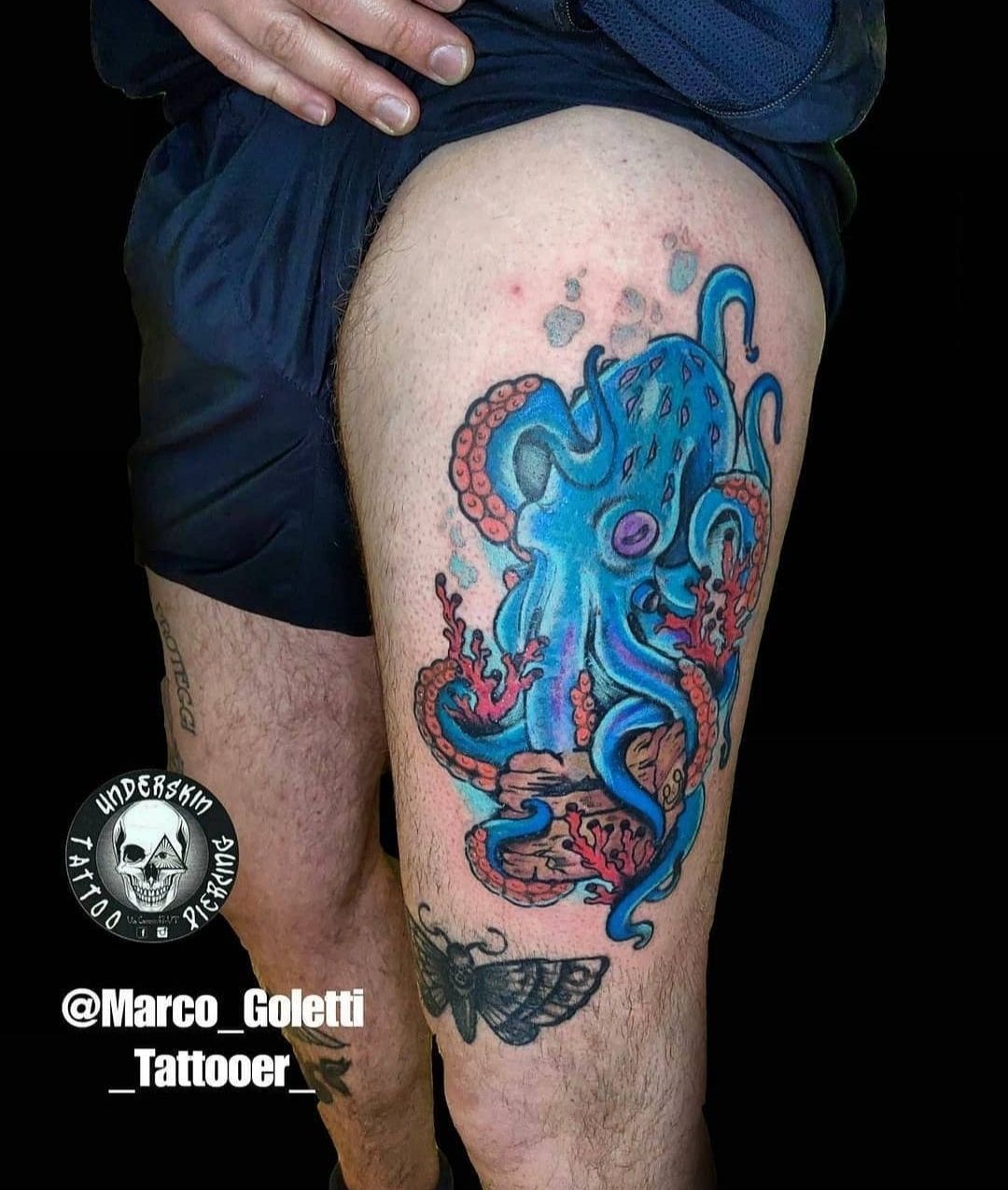 Tatuaggio di un polpo colorato blu e rosa sulla coscia di una persona.