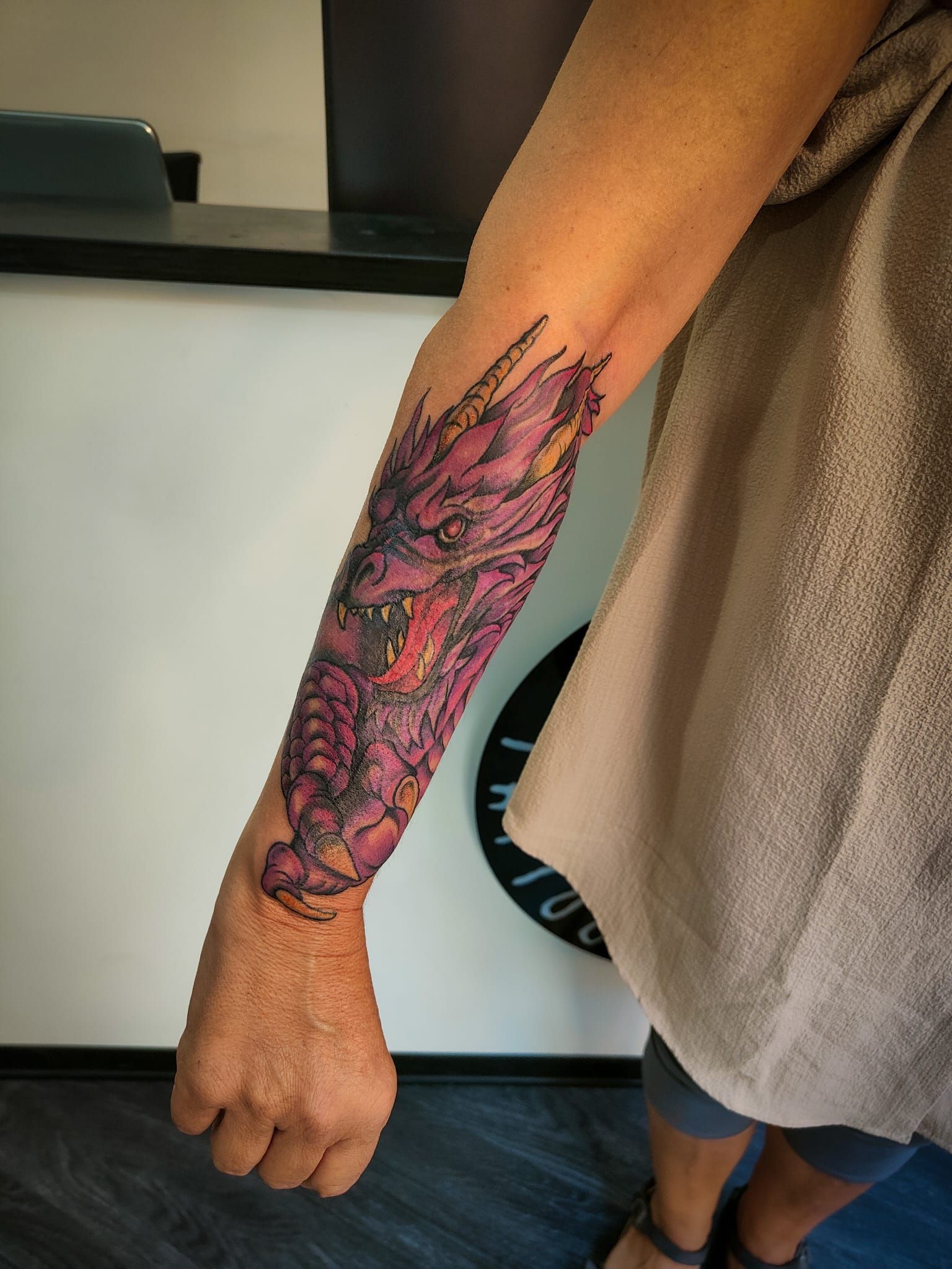 Sull'avambraccio è presente un tatuaggio dettagliato di un drago viola e rosso, ripreso su uno sfondo sfocato in studio.