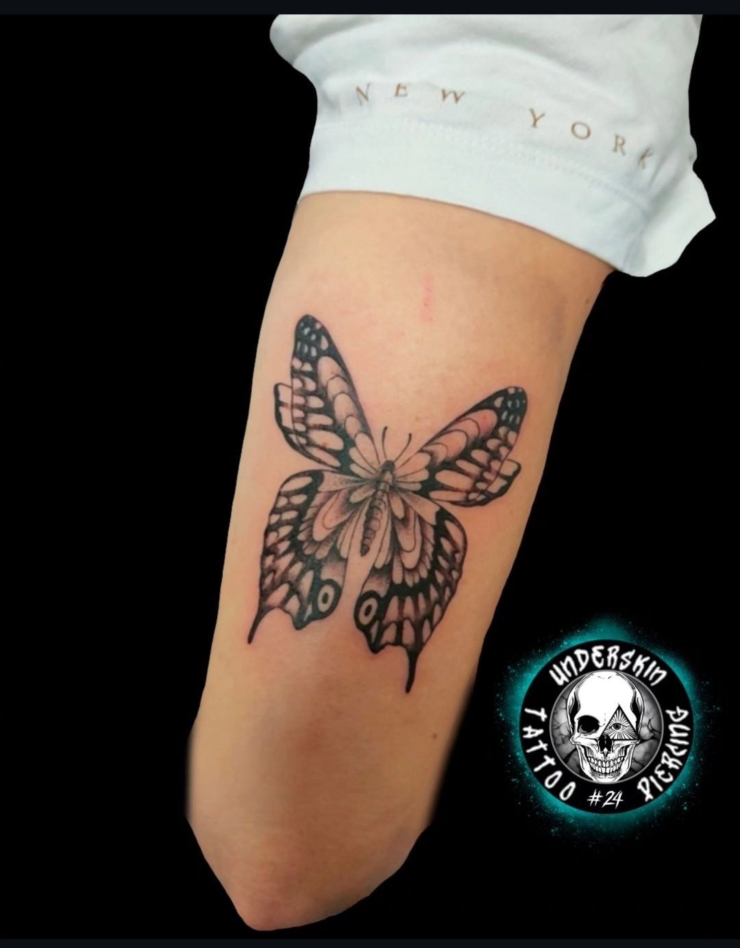 Tatuaggio a forma di farfalla sull'avambraccio, contornato di nero con dettagli rosa su pelle chiara.