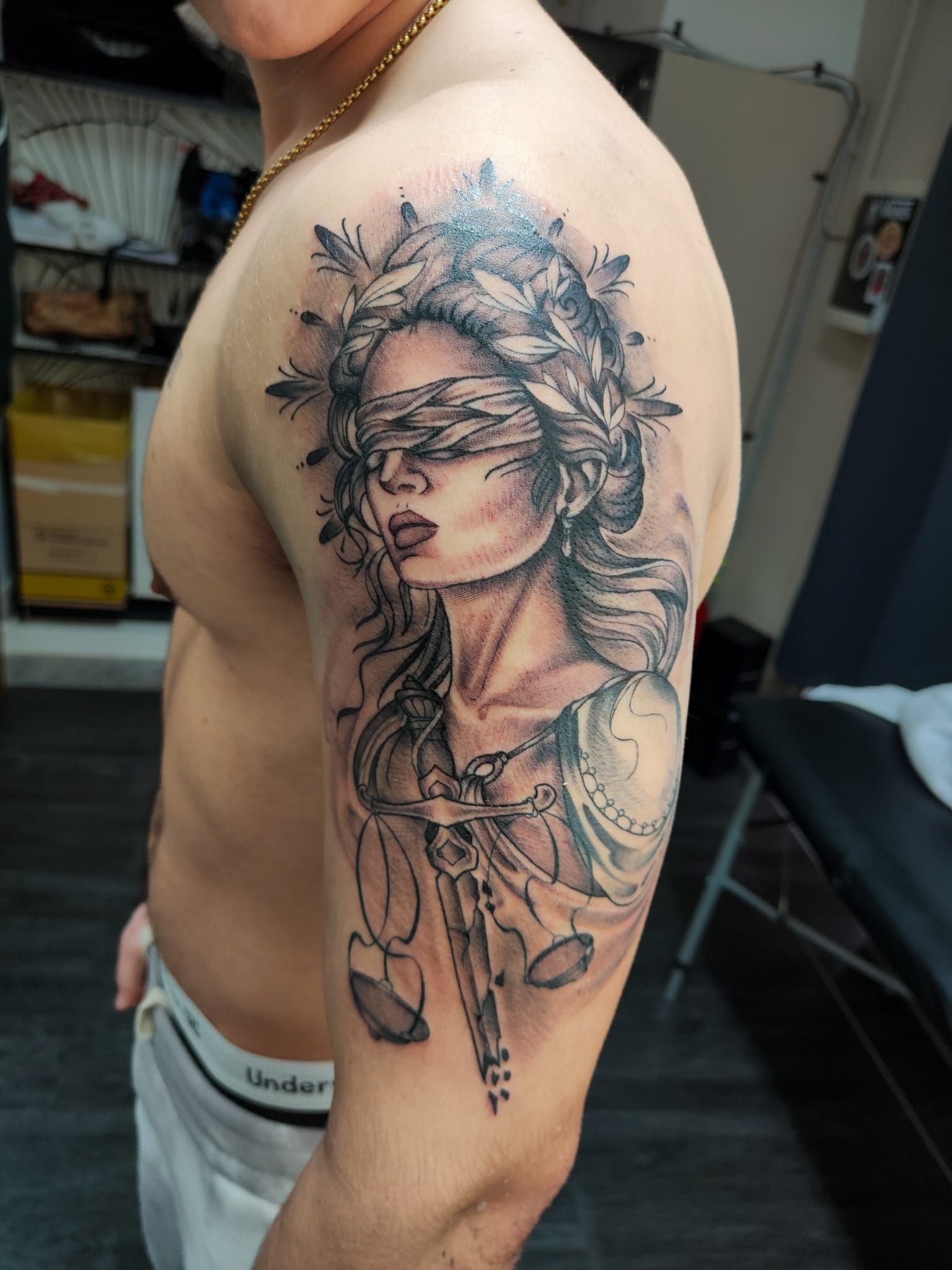 Un tatuaggio in bianco e nero sul braccio raffigurante la dea della giustizia con una benda sugli occhi e una corona d'alloro