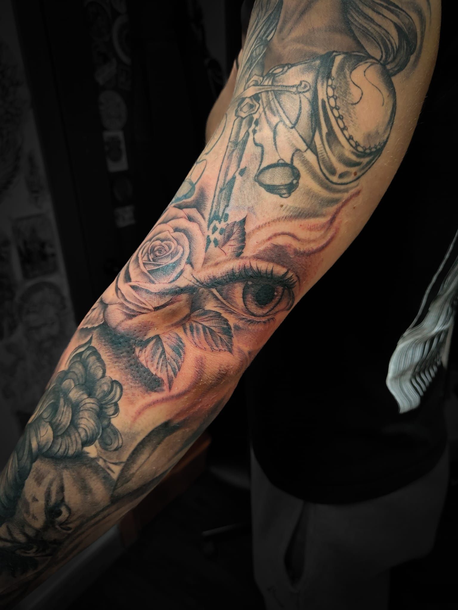 Avambraccio tatuato con motivi floreali e ritratti in bianco e nero su sfondo scuro.