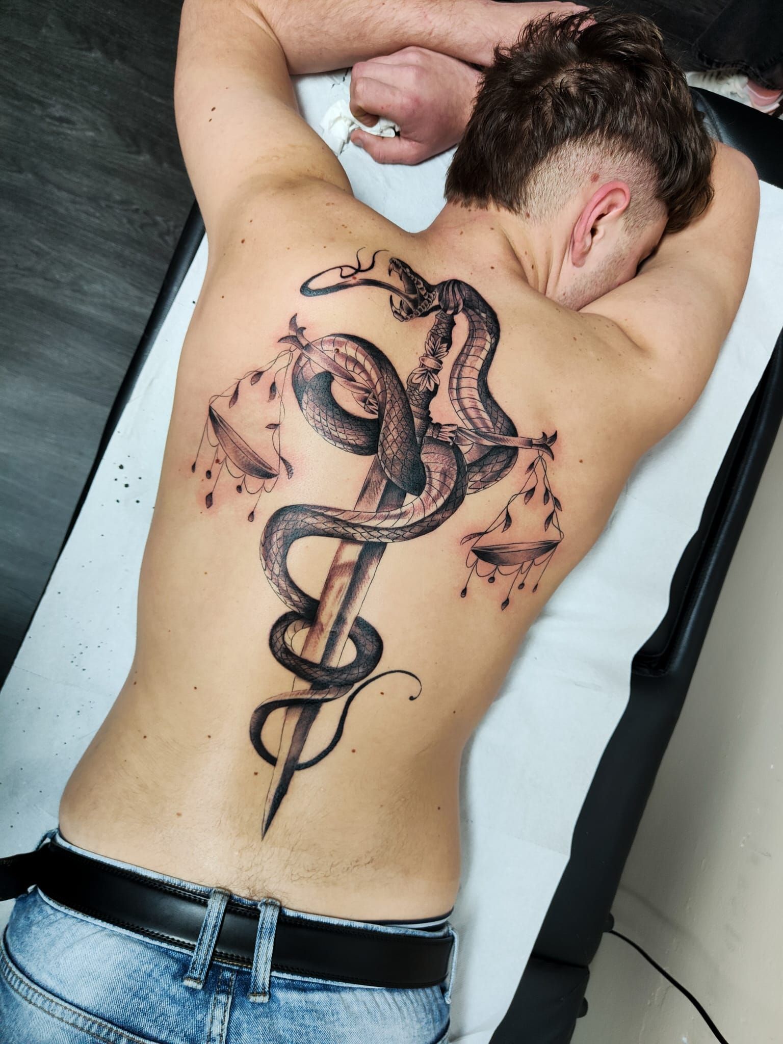 Persona sdraiata a pancia in giù, che mostra un grande tatuaggio di un serpente nero al centro della schiena.