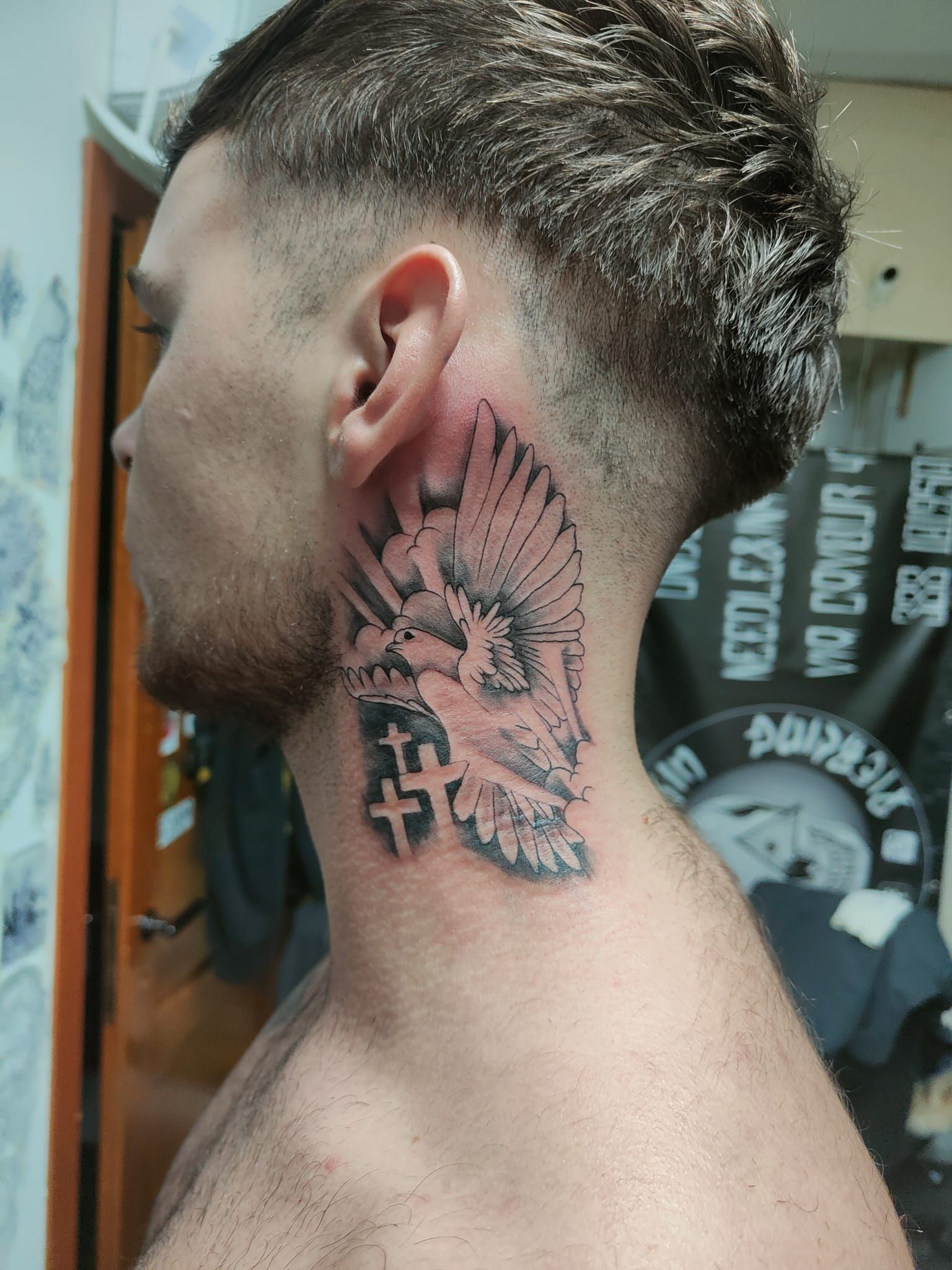 Profilo laterale di una persona con un grande tatuaggio nero e rosa sul collo e un taglio di capelli corto e sfumato.