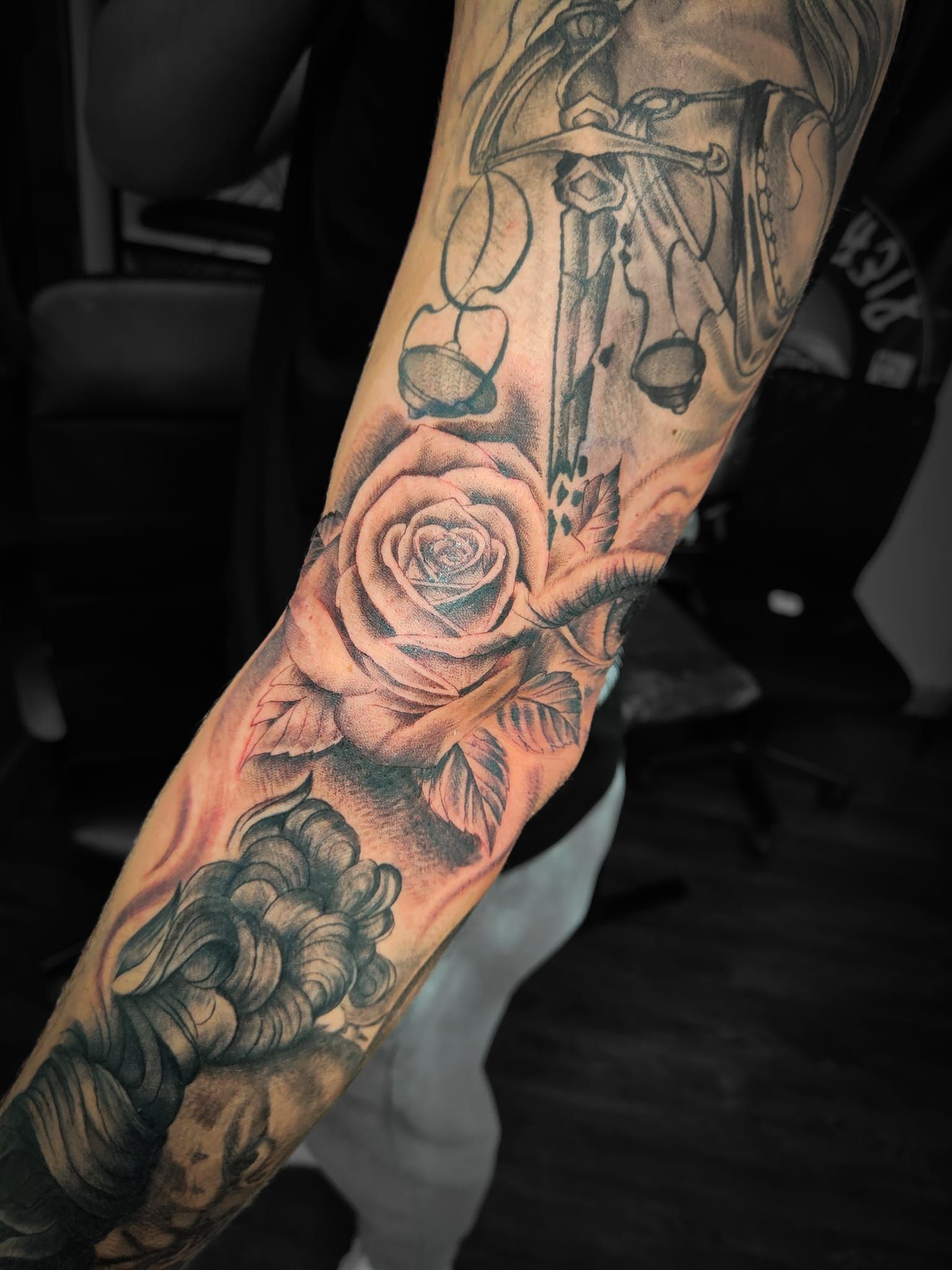Primo piano di un avambraccio tatuato con una rosa e un disegno in stile vintage, realizzati con inchiostro nero e grigio.