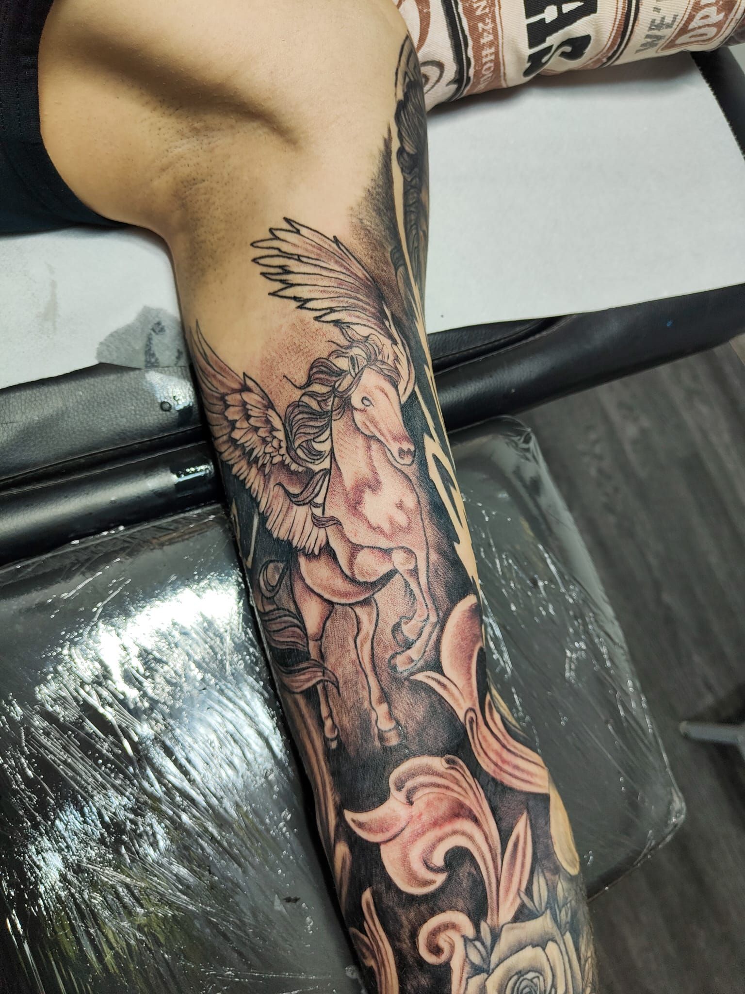 Primo piano di una manica di tatuaggi colorati su un braccio, che mostra disegni floreali e un cavallo alato.