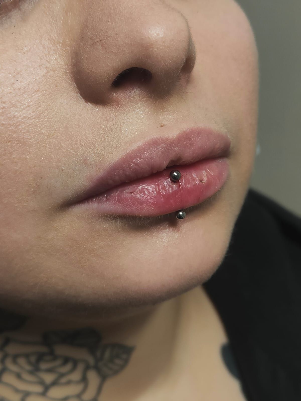 Primo piano della parte inferiore del viso con un piercing nero al labbro e un tatuaggio floreale sul collo.