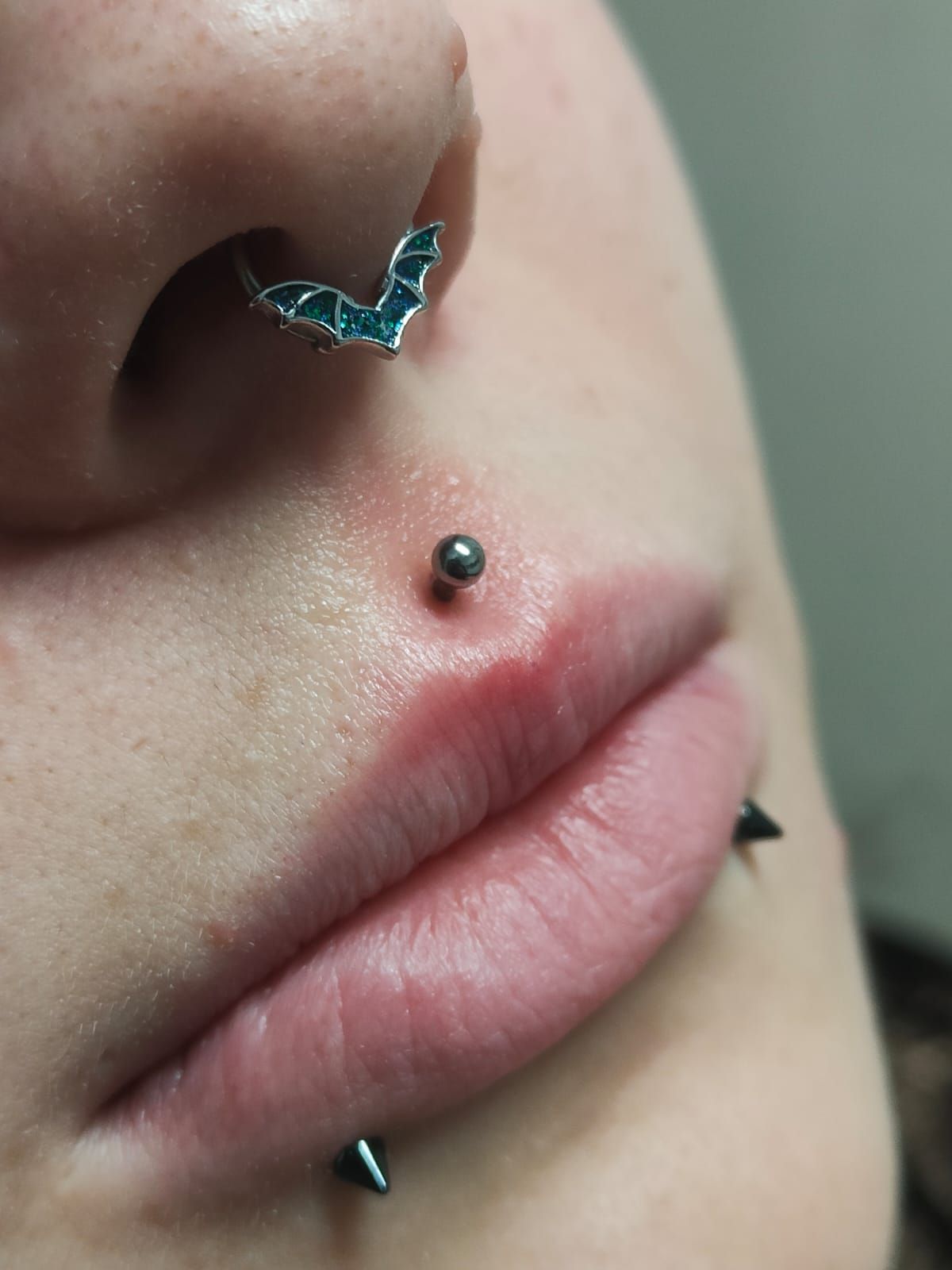 Primo piano di naso e labbra con molteplici piercing facciali, tra cui un anello al naso a forma di farfalla.