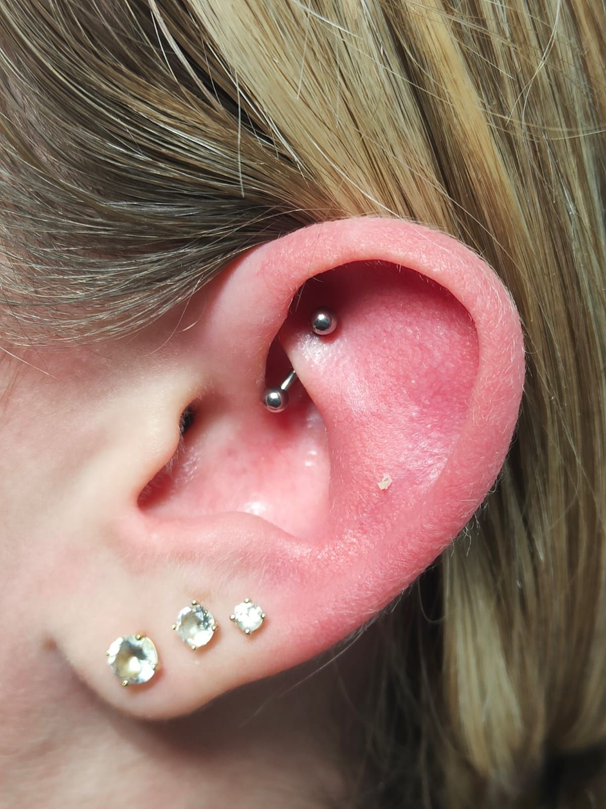 Primo piano di un orecchio con piercing multipli e tre piccoli orecchini a perno nel lobo.