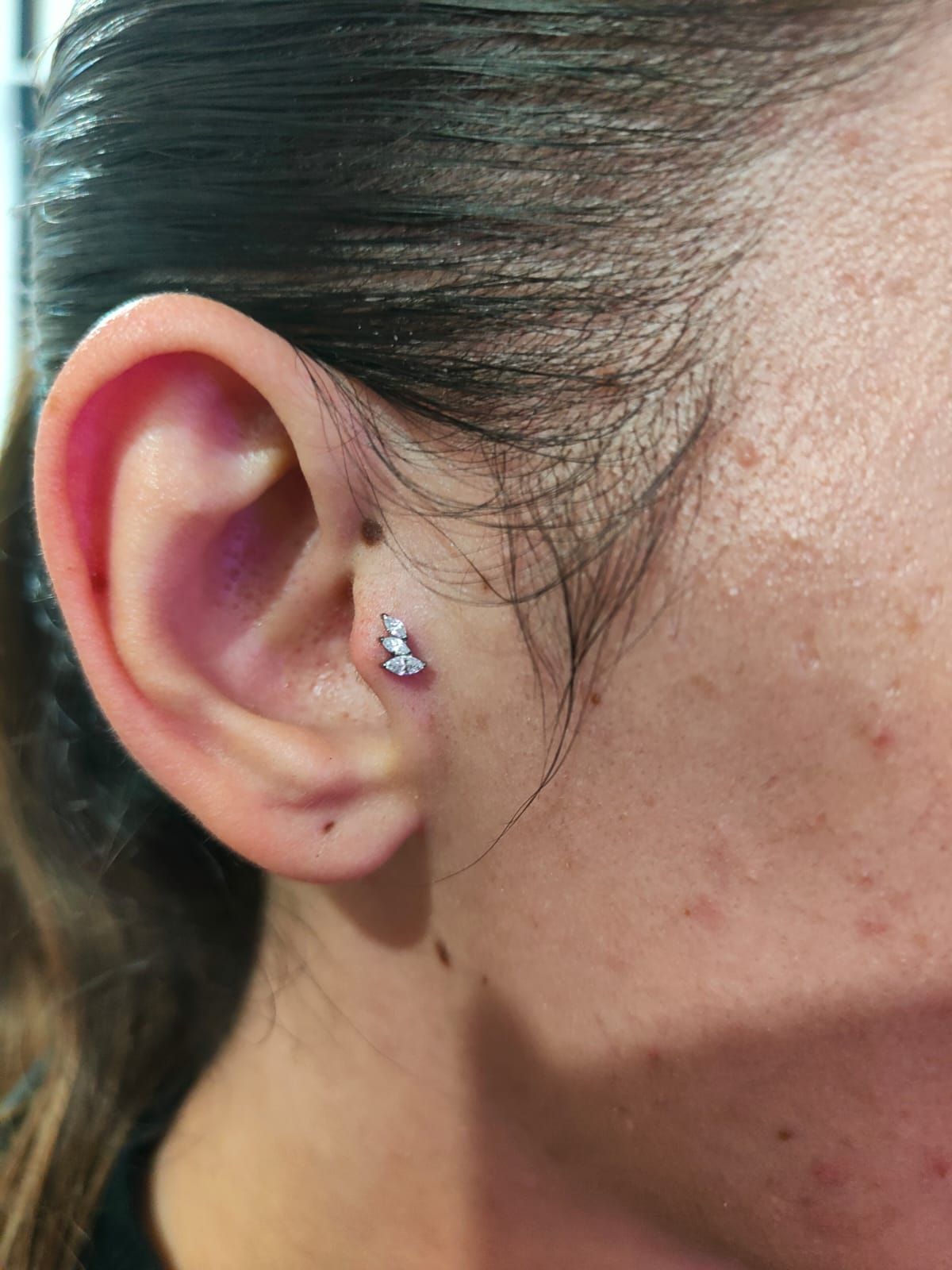 Primo piano dell'orecchio di una persona con un piccolo orecchino a perno e i capelli scuri tirati indietro.
