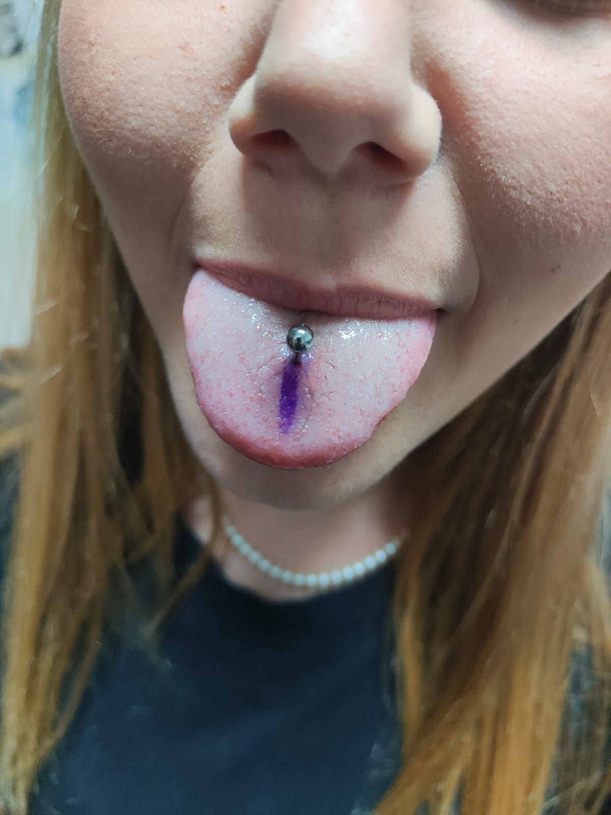 Primo piano di un piercing alla lingua con tintura viola visibile sulla lingua e sul naso di una persona.