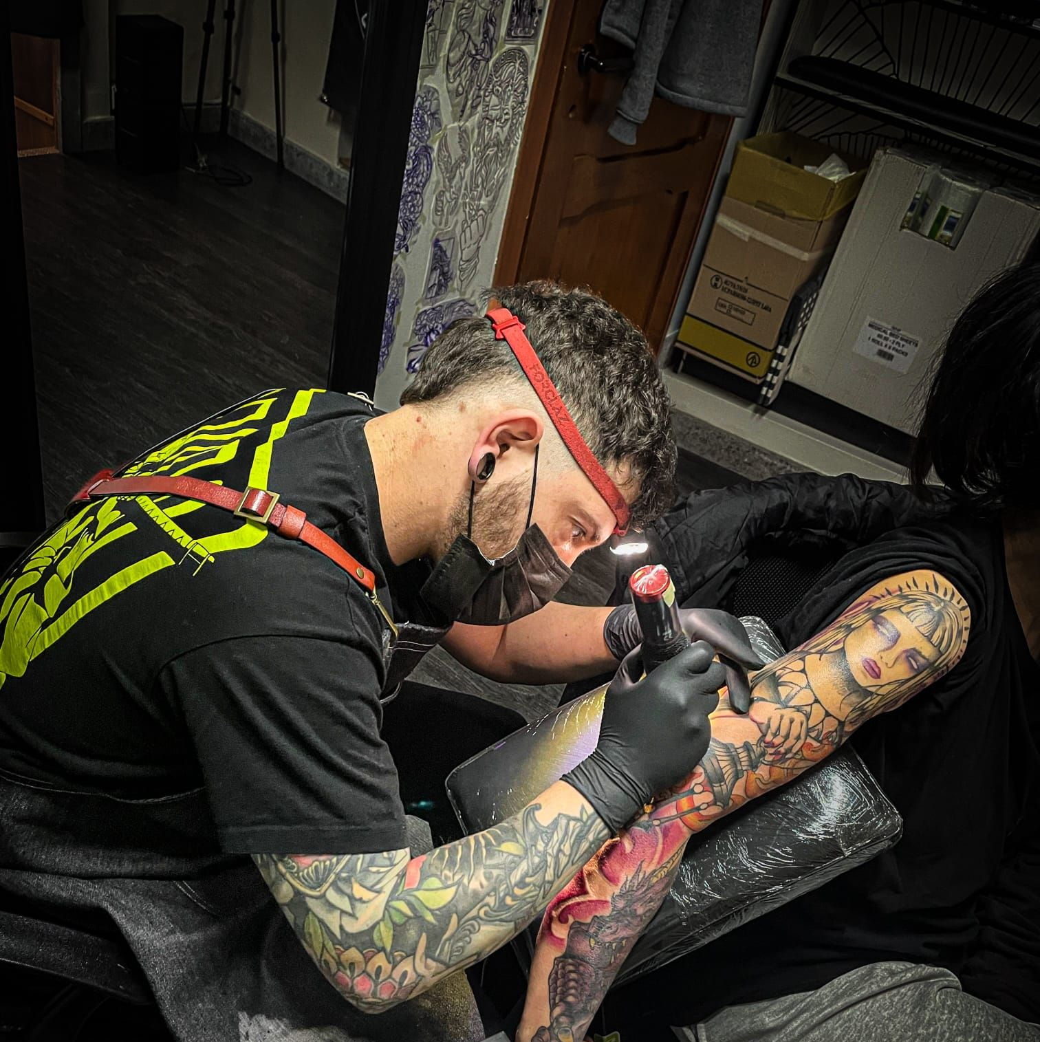 Un primo piano di una mano guantata che utilizza una macchinetta per tatuaggi che crea un disegno dettagliato su un braccio.