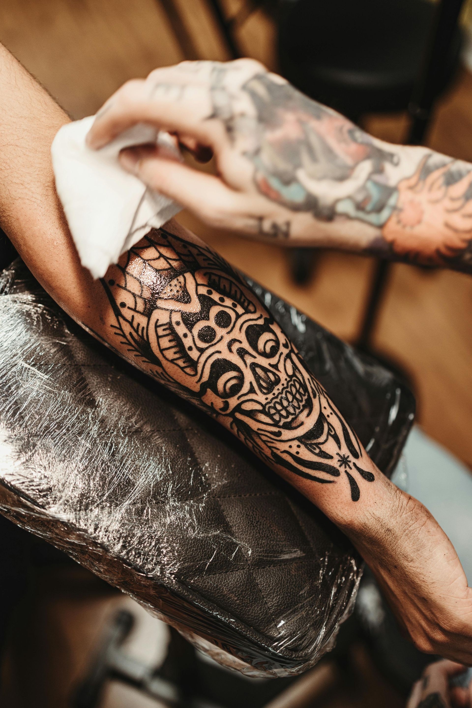 Tatuatore che esegue un tatuaggio nero sull'avambraccio di un cliente seduto su un bracciolo imbottito.