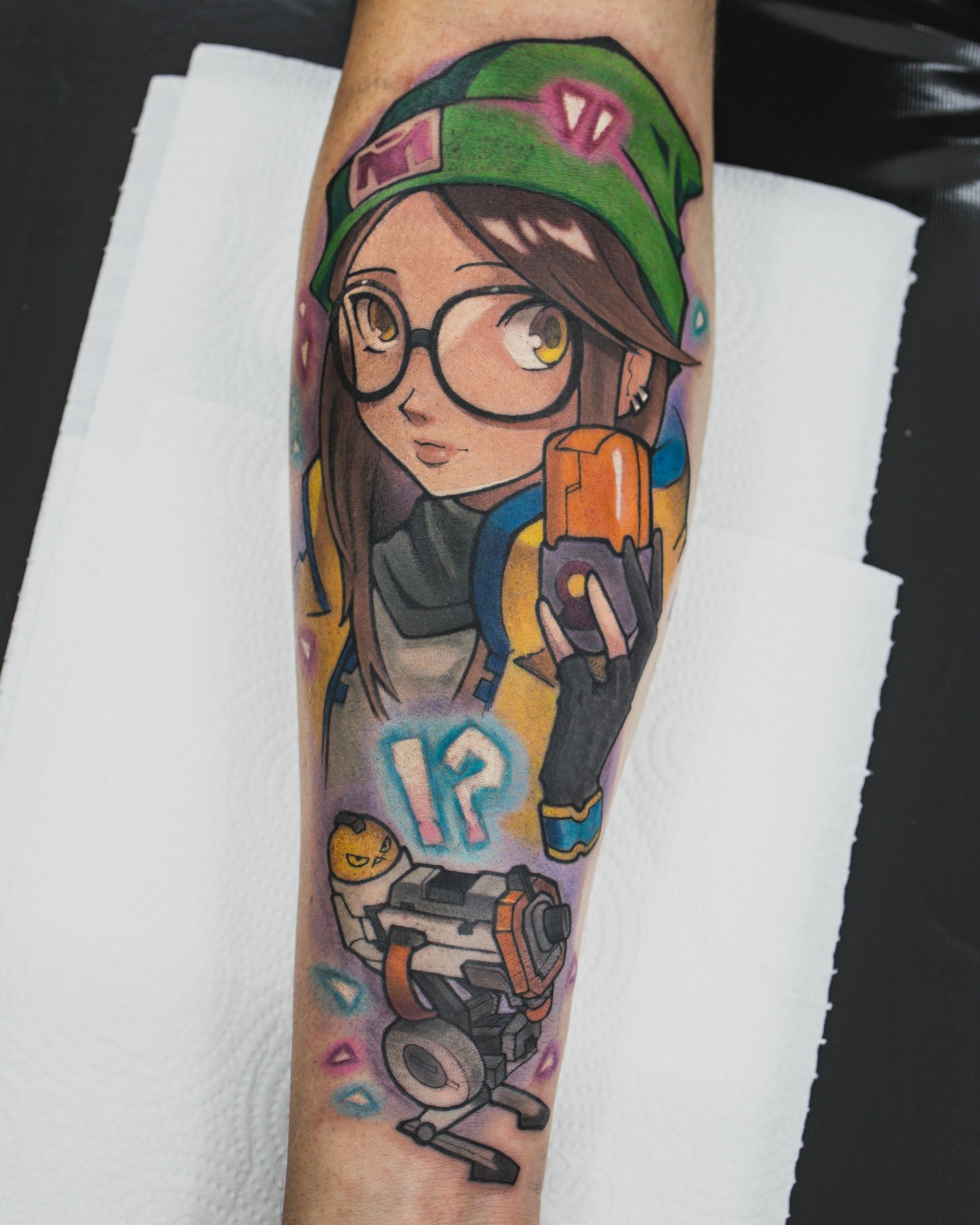 Tatuaggio colorato di un personaggio dei cartoni animati con occhiali e cappello verde che tiene in mano un oggetto arancione