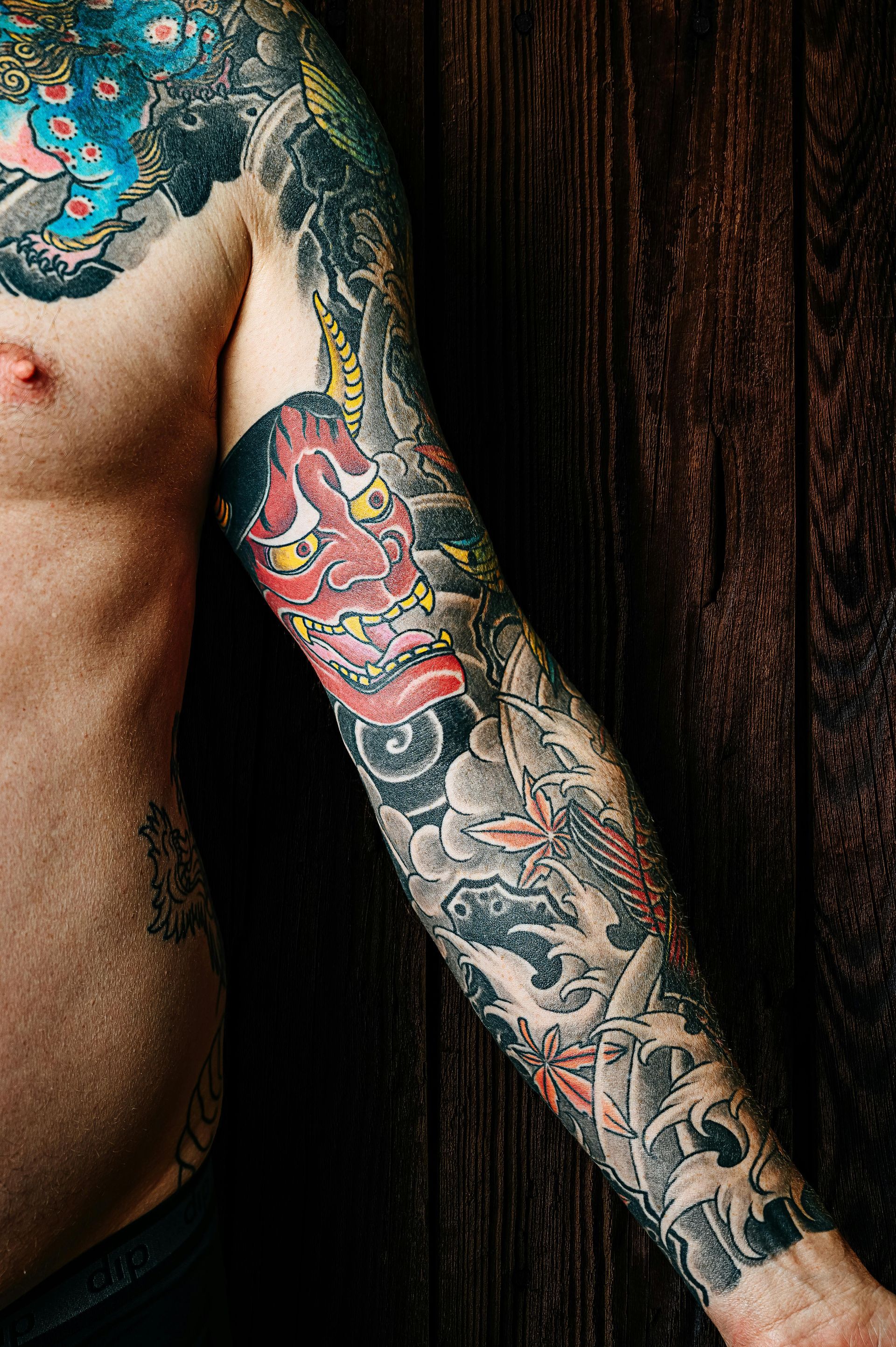 Il braccio e la spalla con un tatuaggio tradizionale giapponese raffigurante una maschera Hannya rossa, onde e foglie.