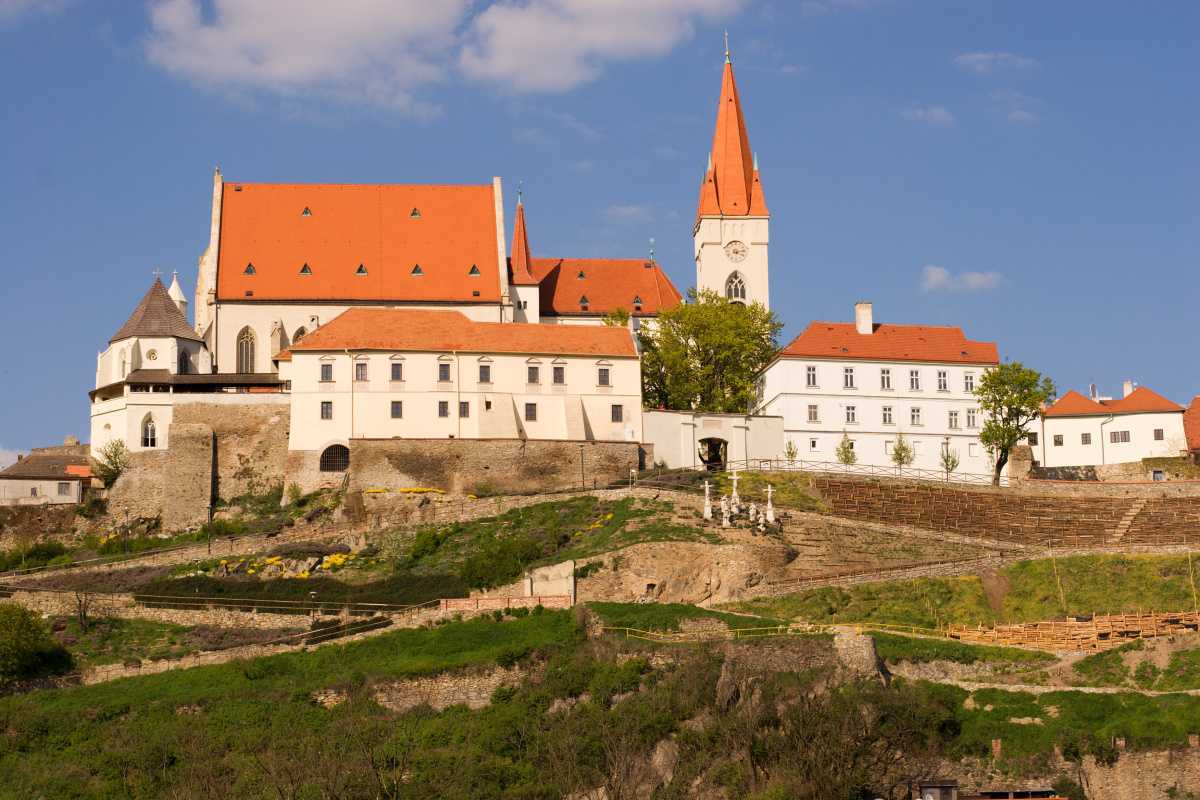 Hrad na vrcholu kopce s kostelem v pozadí.