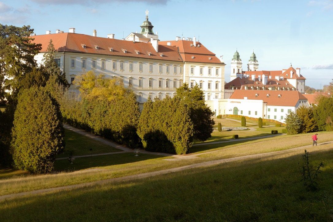 Velká budova s červenou střechou je obklopena stromy a trávou.
