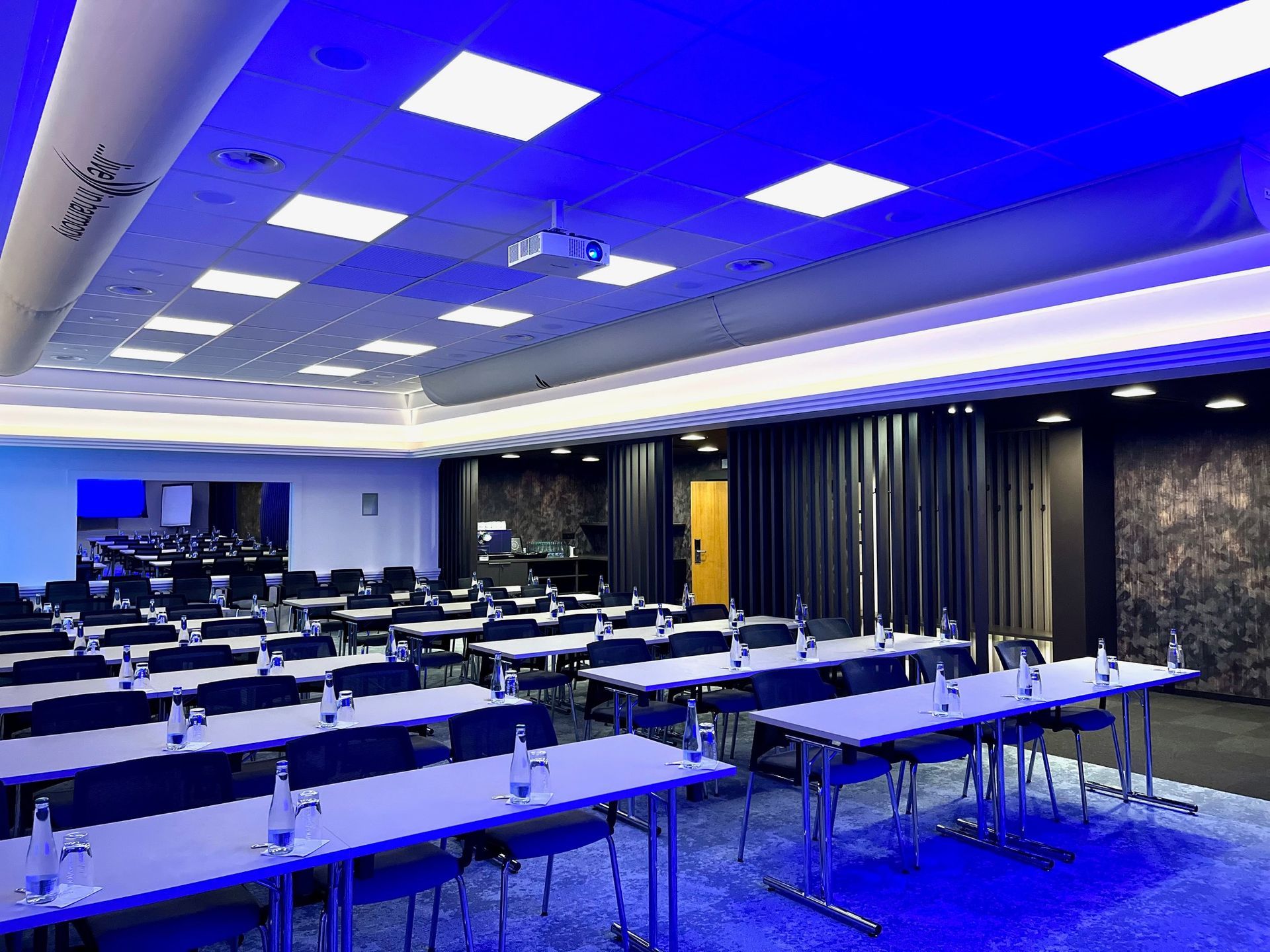 Konferenční místnost se stoly a židlemi a projektorem na stropě.