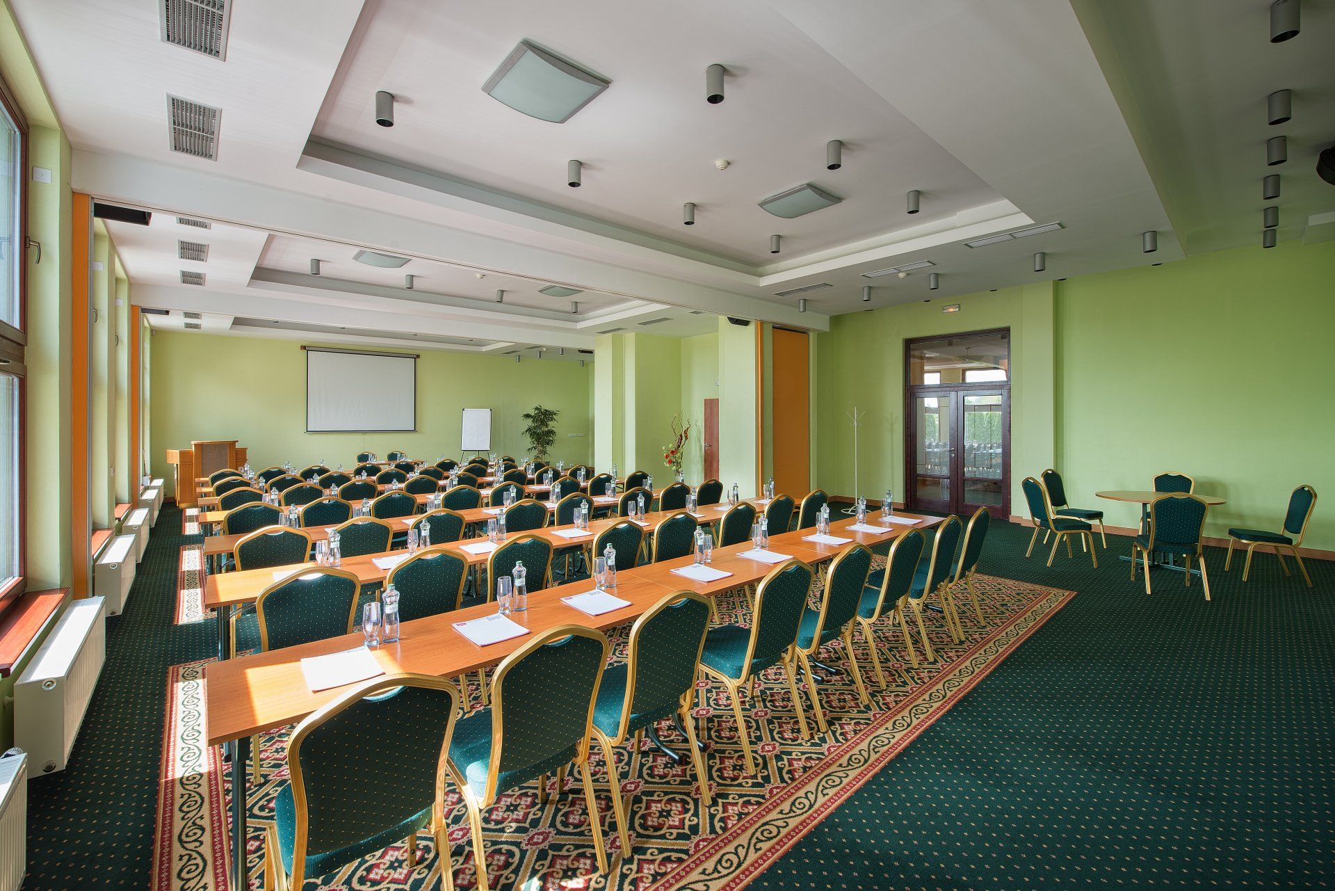 Velká konferenční místnost se stoly a židlemi a promítacím plátnem.