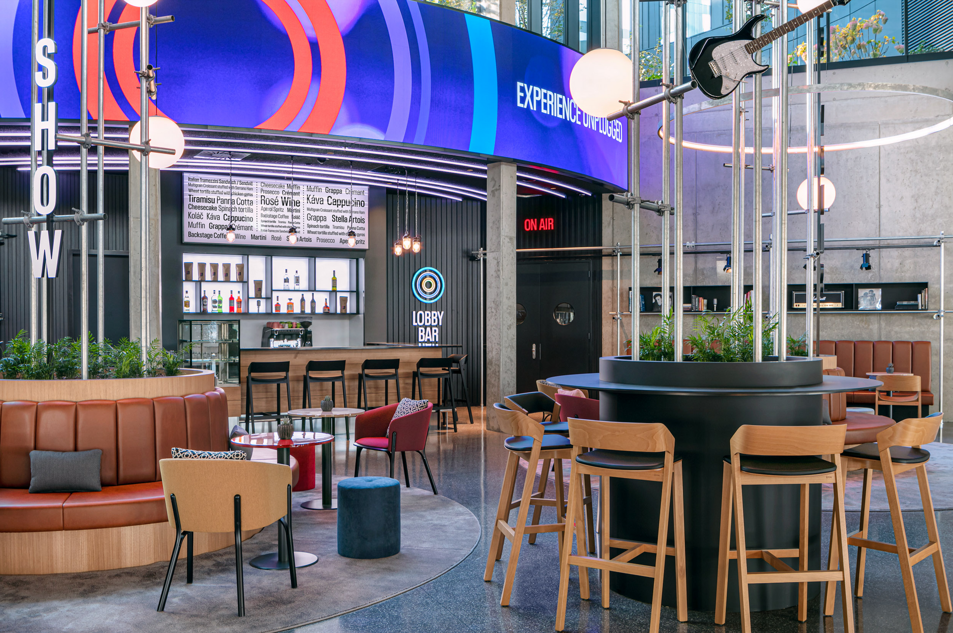 Restaurace se stoly a židlemi před velkoplošnou obrazovkou.