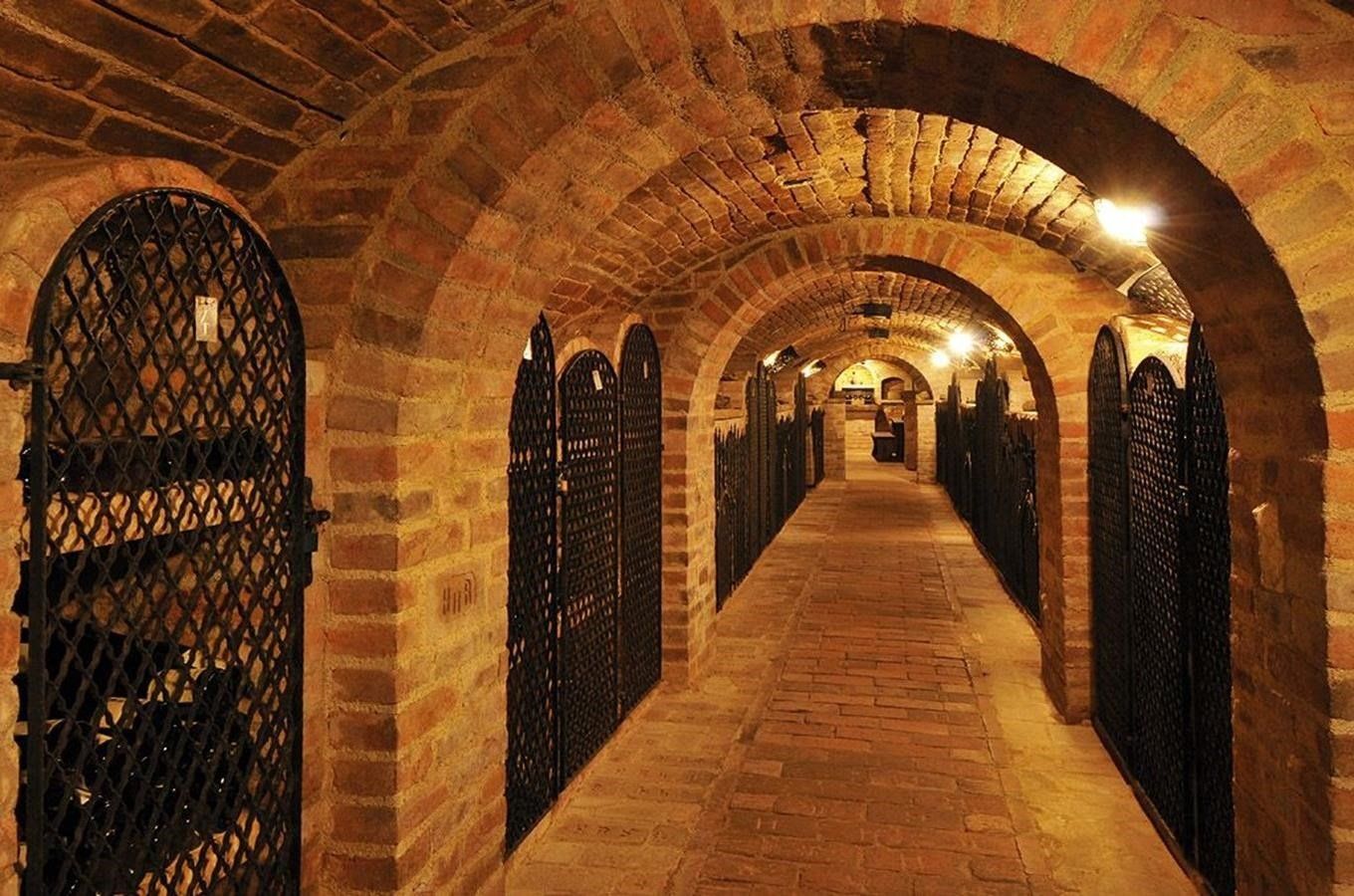 Dlouhý cihlový tunel s oblouky a plotem ve vinném sklepě.