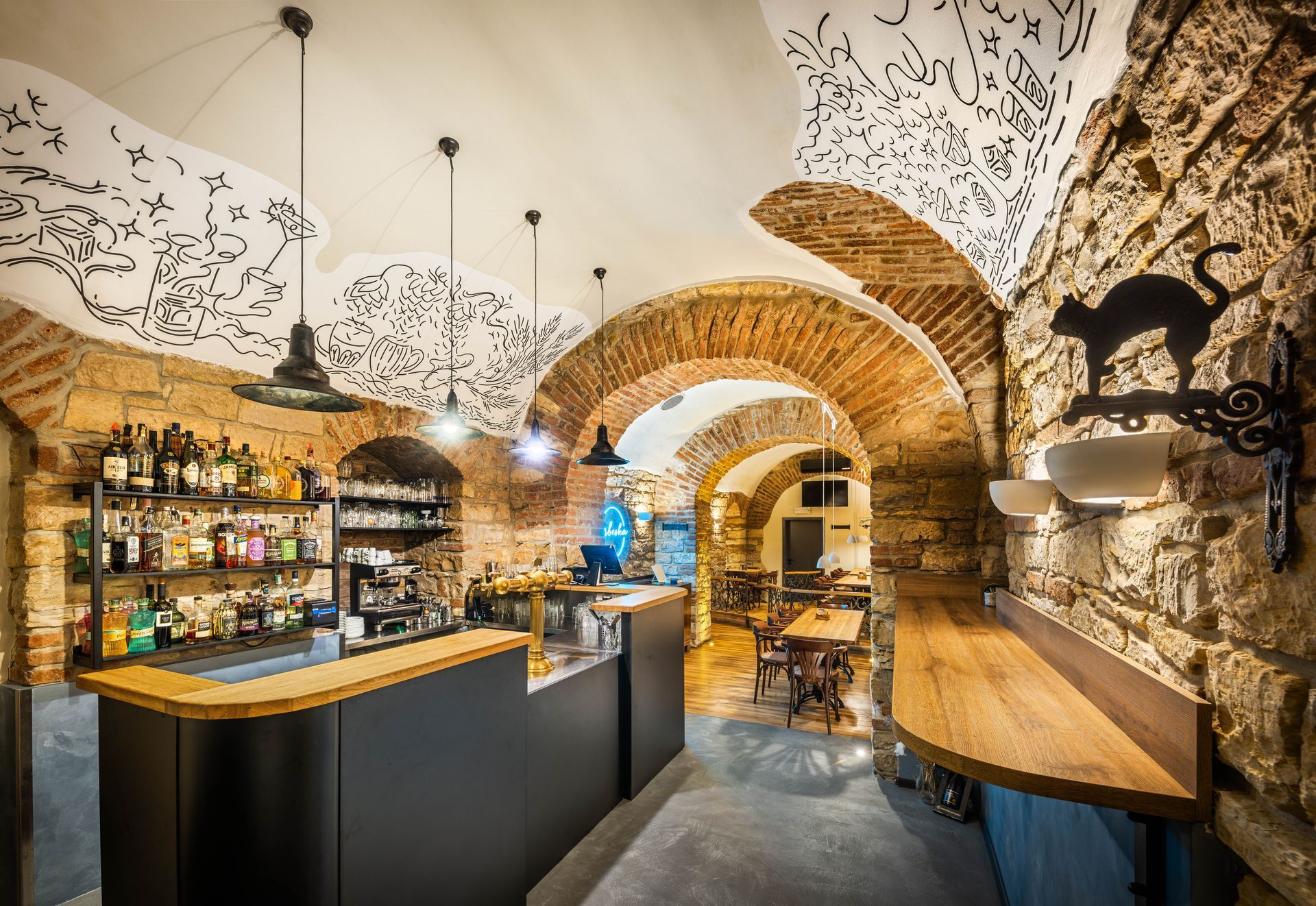 Restaurace s klenutými stropy a černou kočkou na zdi.