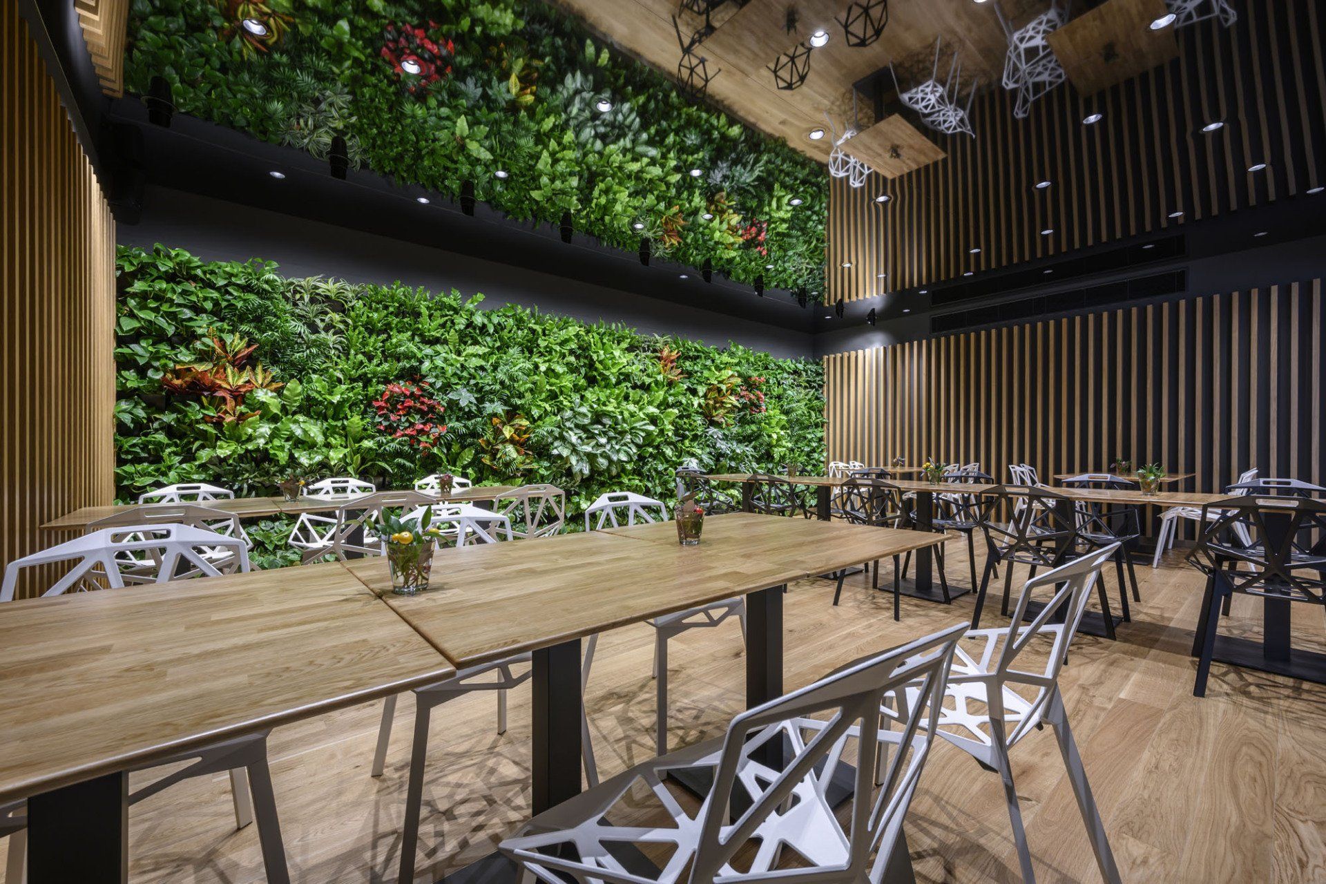 Restaurace se stoly a židlemi a zelenou stěnou.