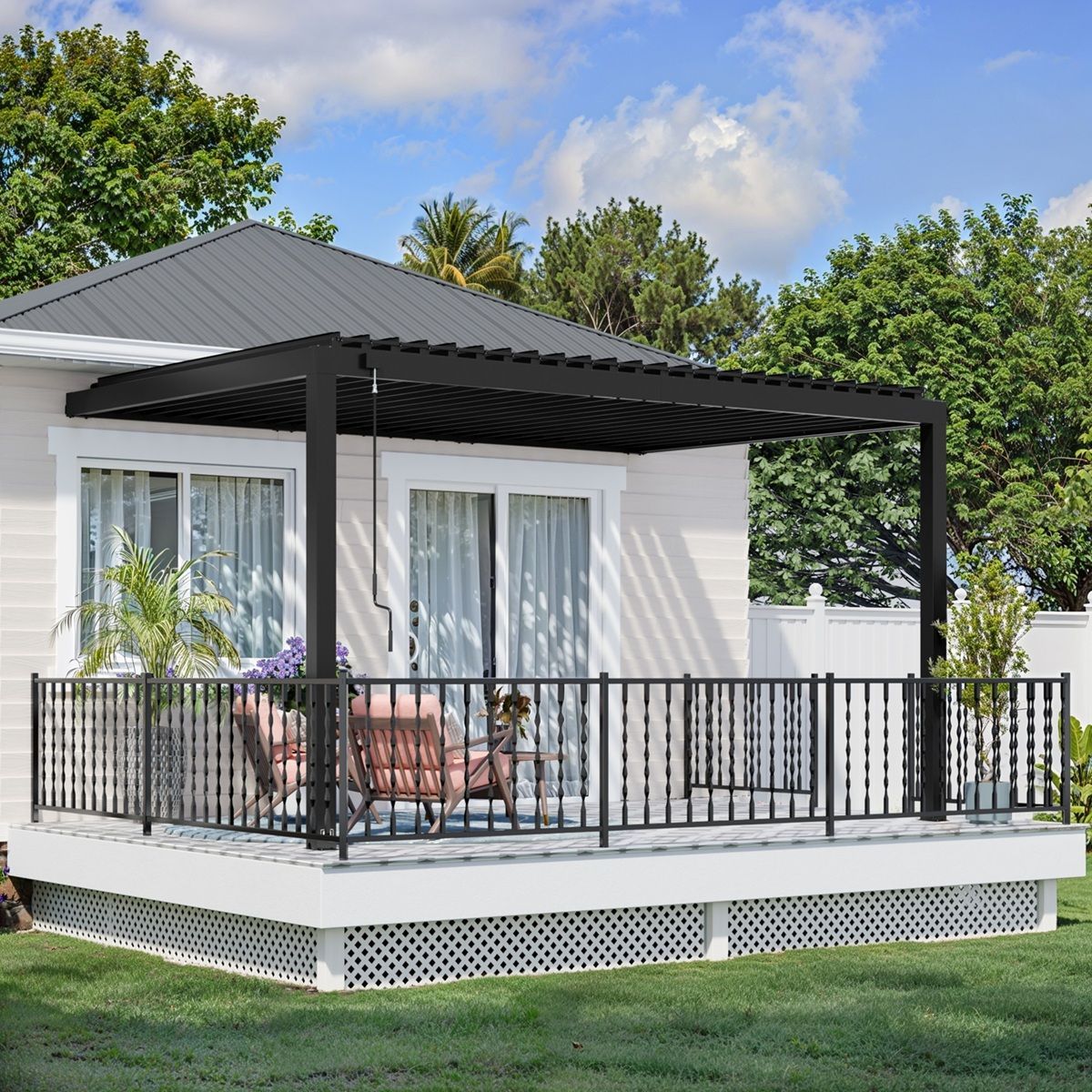 White house porch with black railing and pergola, furnished with outdoor chairs and set on a green lawn.