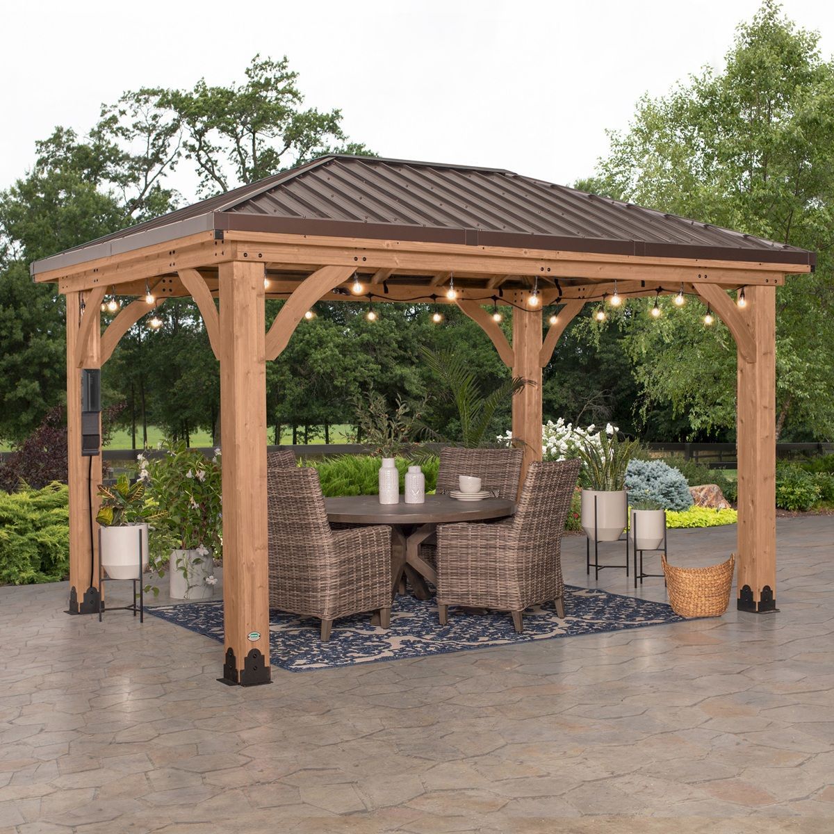 Wooden gazebo with wicker chairs and string lights on a wet patio, surrounded by potted plants
