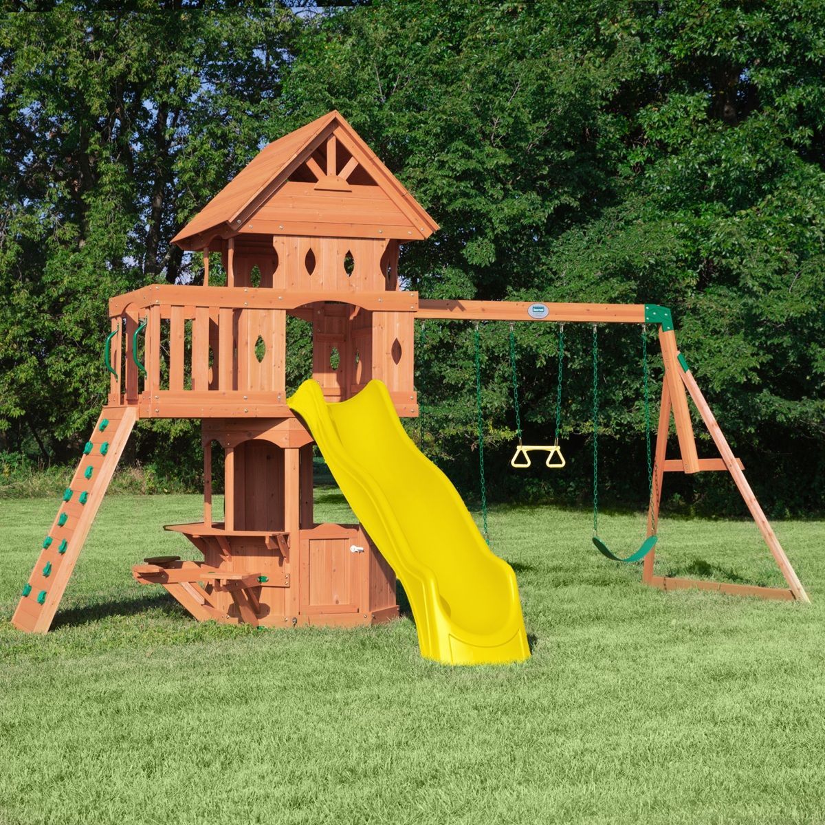 Wooden backyard playset with bright yellow slide, swings, and ladder on a grassy lawn.
