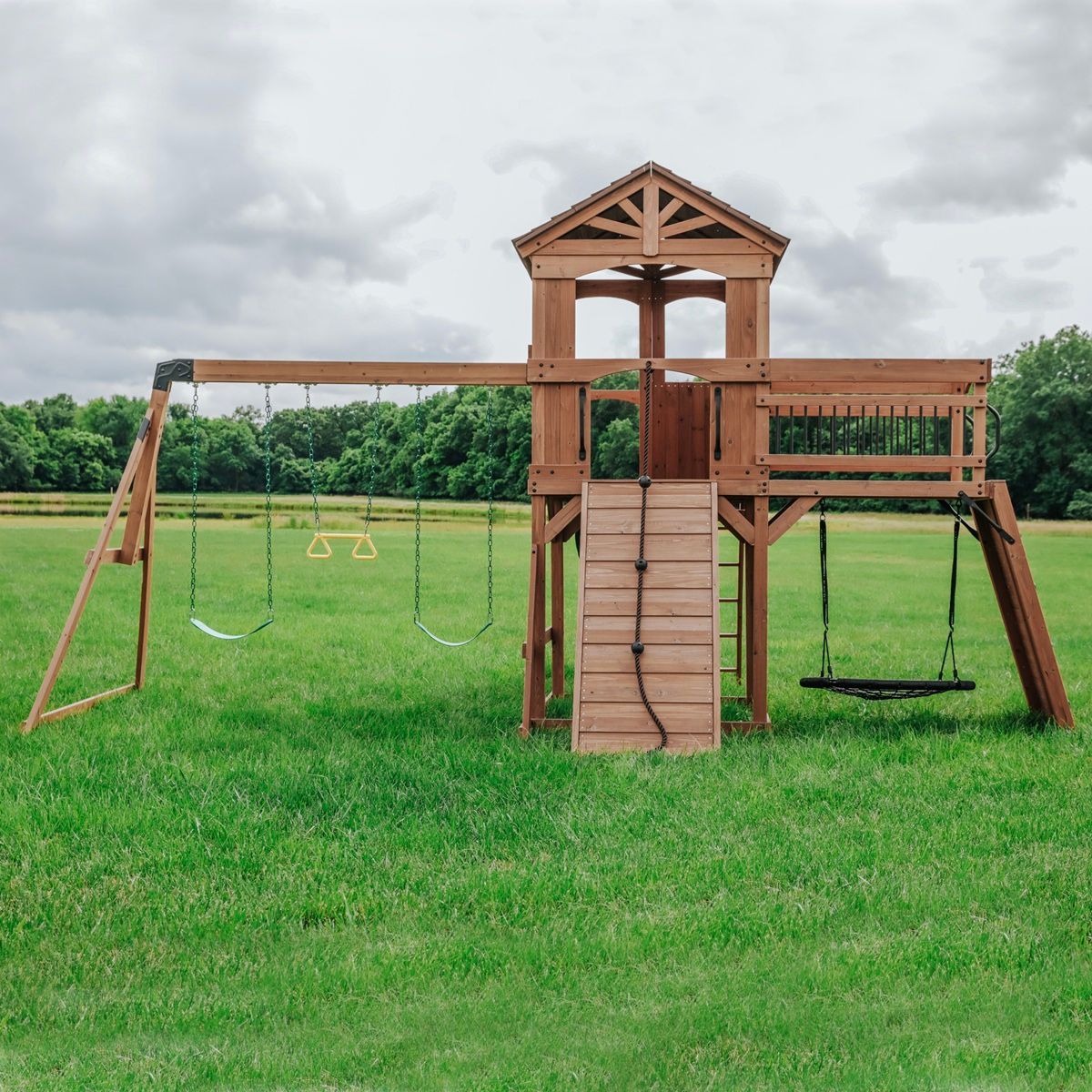 Wooden playground set with swings and climbing platform in a grassy field under cloudy sky