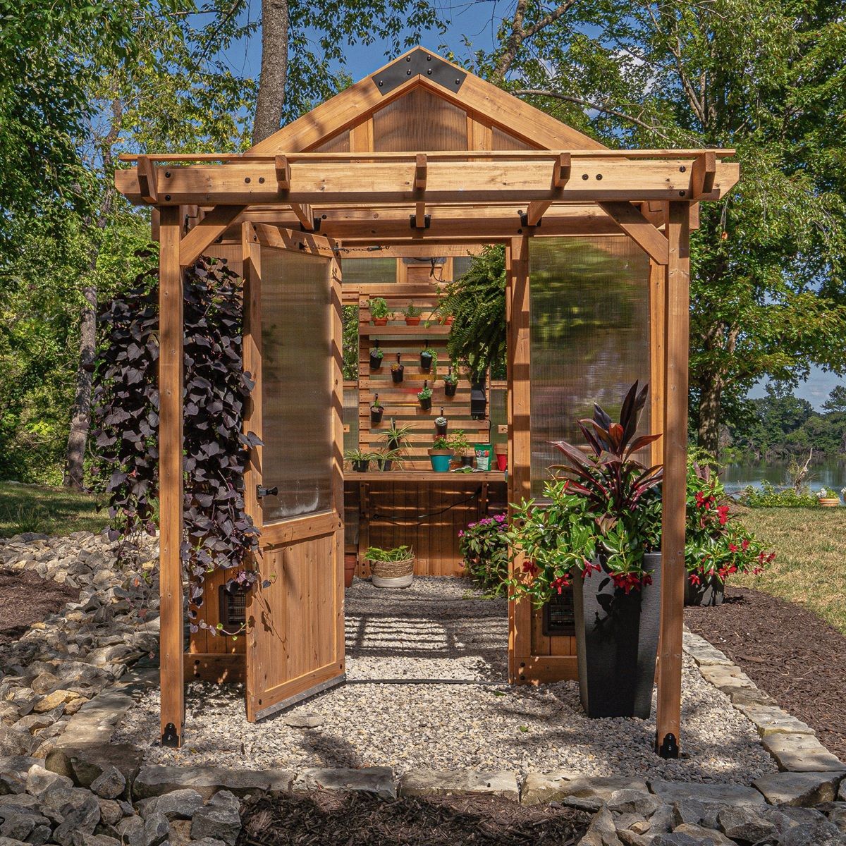Wooden garden greenhouse with open door, stone path, and potted flowers in bright sunlight