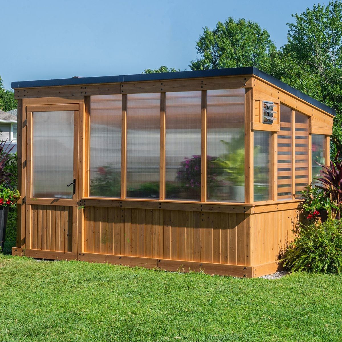 Wooden backyard greenhouse with large windows and a dark roof on a grassy lawn.