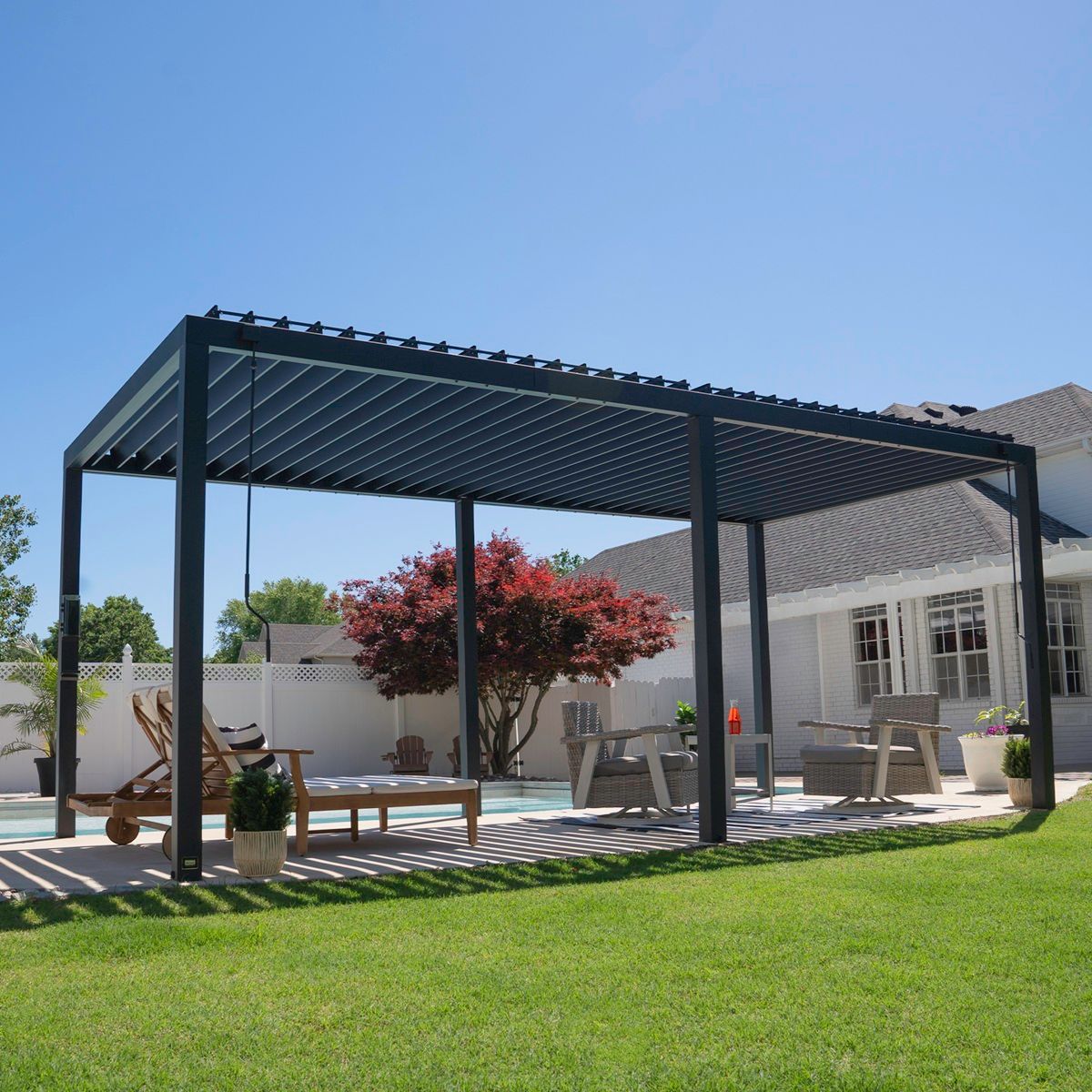 Modern backyard patio with a black pergola, seating area, and green lawn under a blue sky
