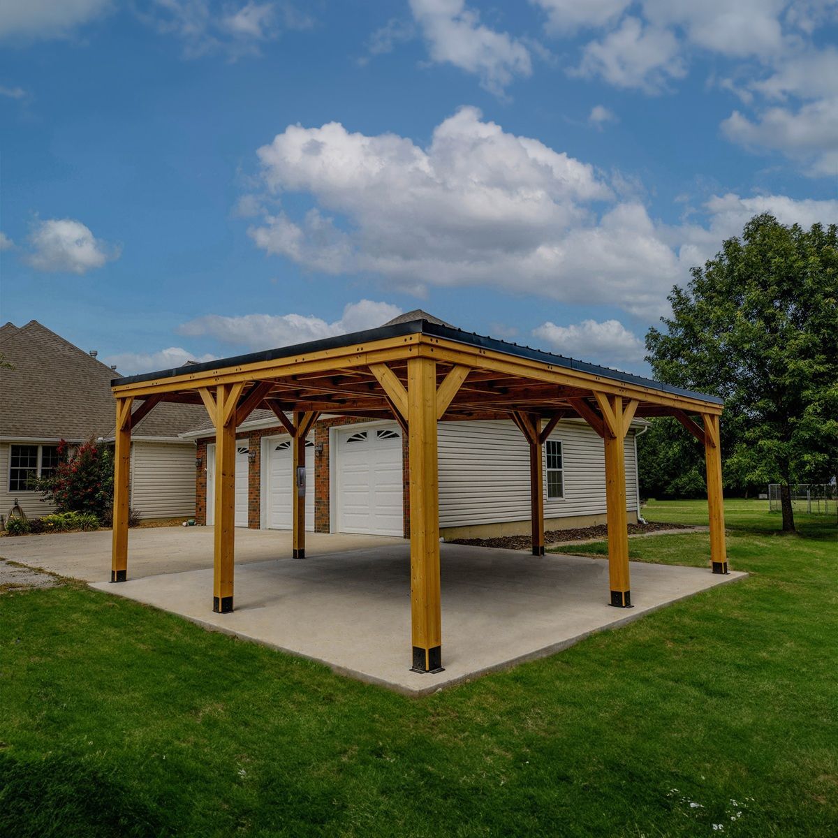 Wooden open-air pavilion with white walls on a concrete pad, surrounded by green grass under a blue sky