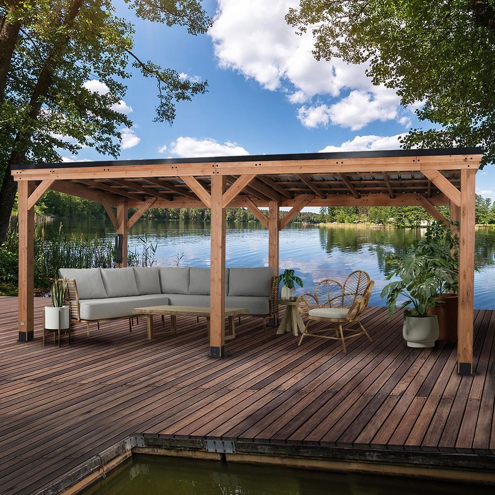 Wooden lakeside deck with pergola, sofa, chairs, and potted plants under a blue sky