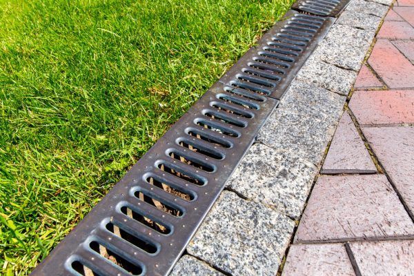 Black metal drain grate beside grass and a brick walkway, with a concrete curb.