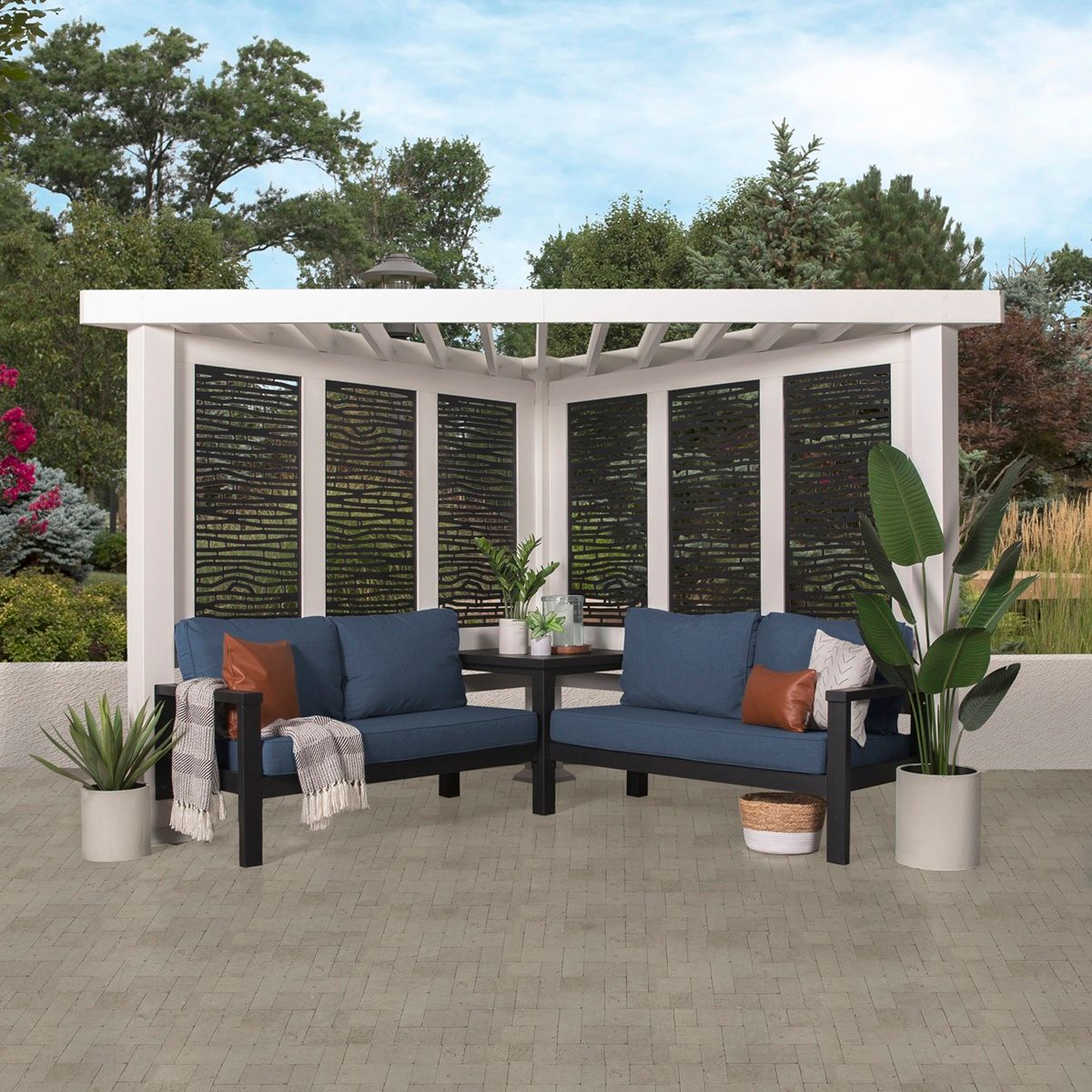 White pergola with blue cushioned benches, potted plants, and dark privacy screens on a patio