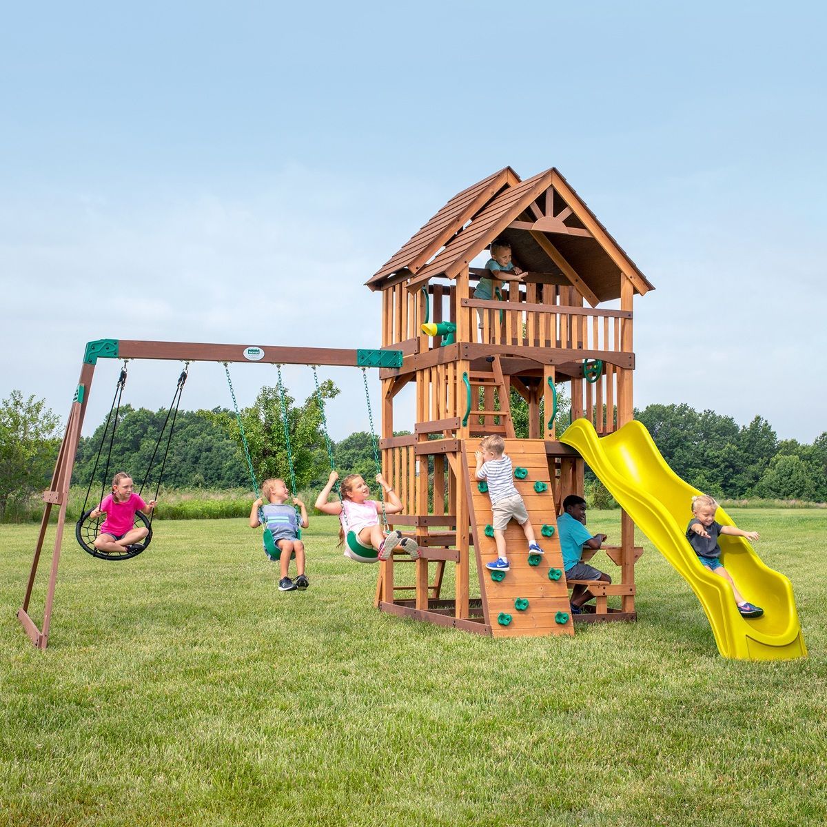 Wooden backyard playset with slide, swings, and children playing on a grassy field
