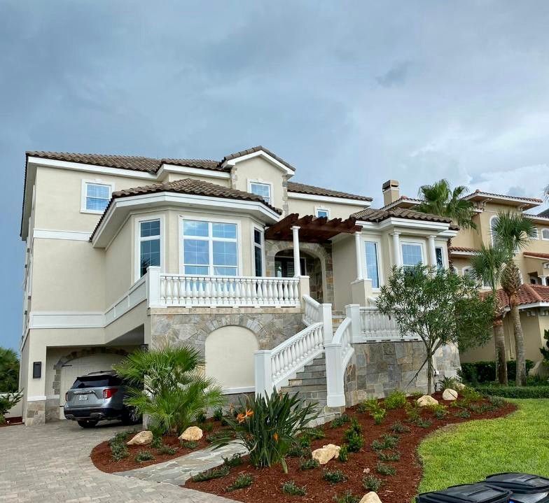 Two-story cream house with white trim, front staircase, balcony, and a car parked in the driveway